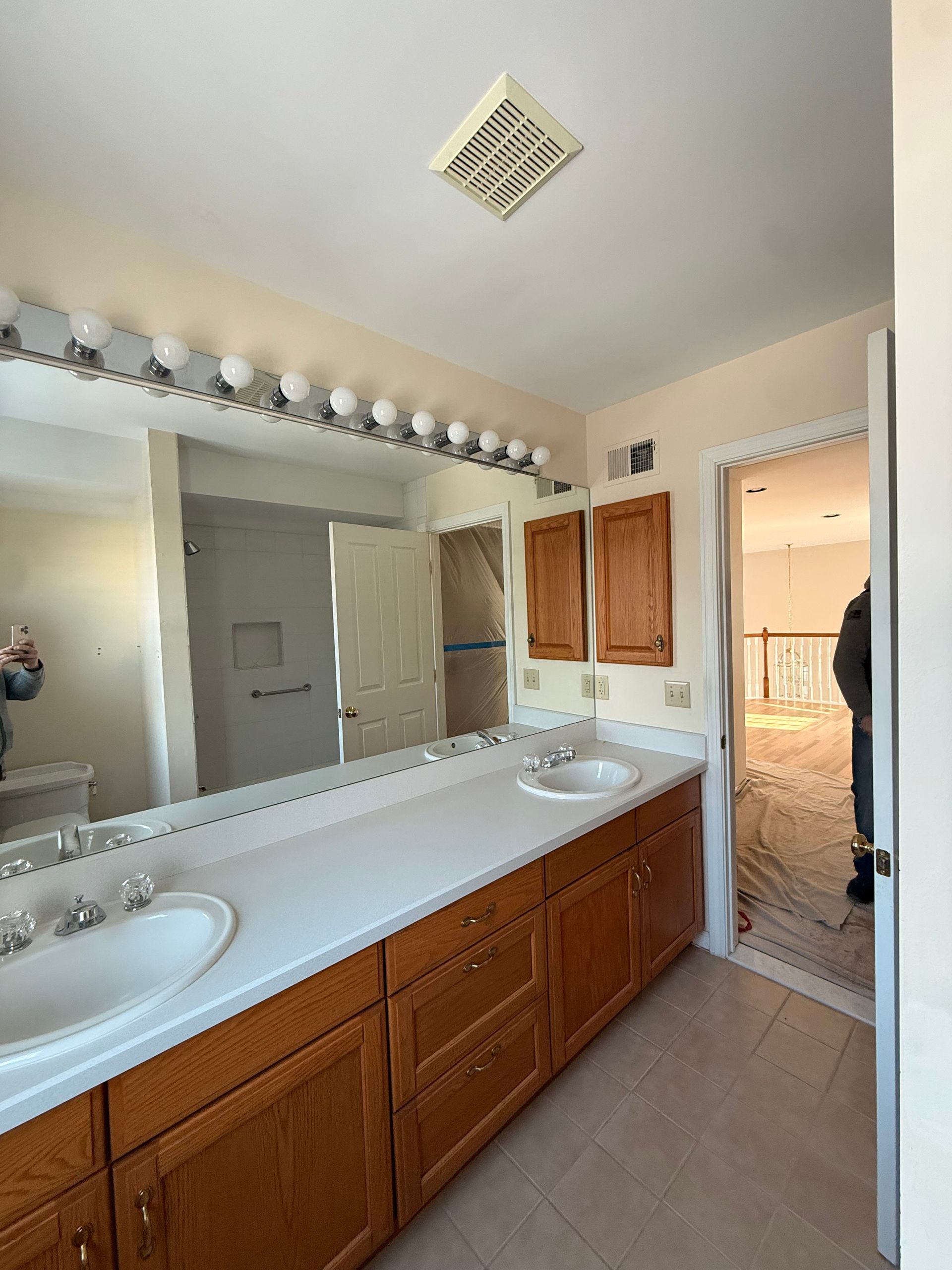 Bathroom with double sink vanity, large mirror, and wooden cabinets beside a shower stall.