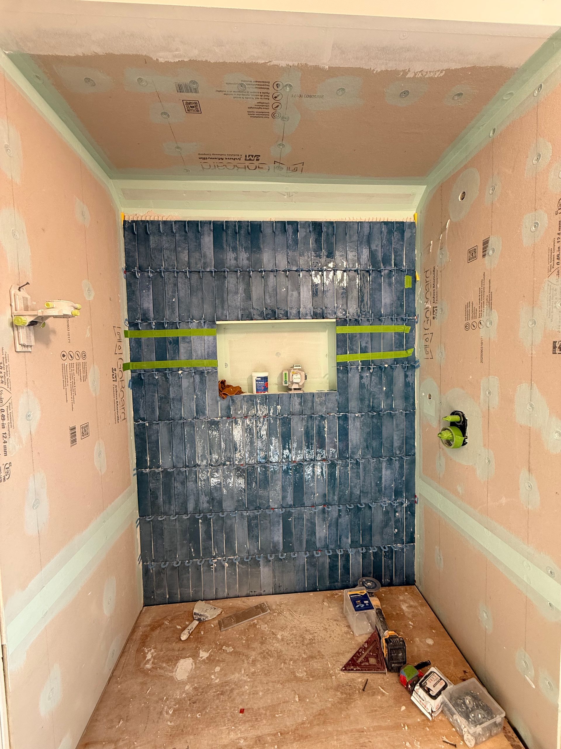 An unfinished shower stall with Cromwell, CT with dark blue tiled back wall, recessed niche, green waterproof board, and construction tools.