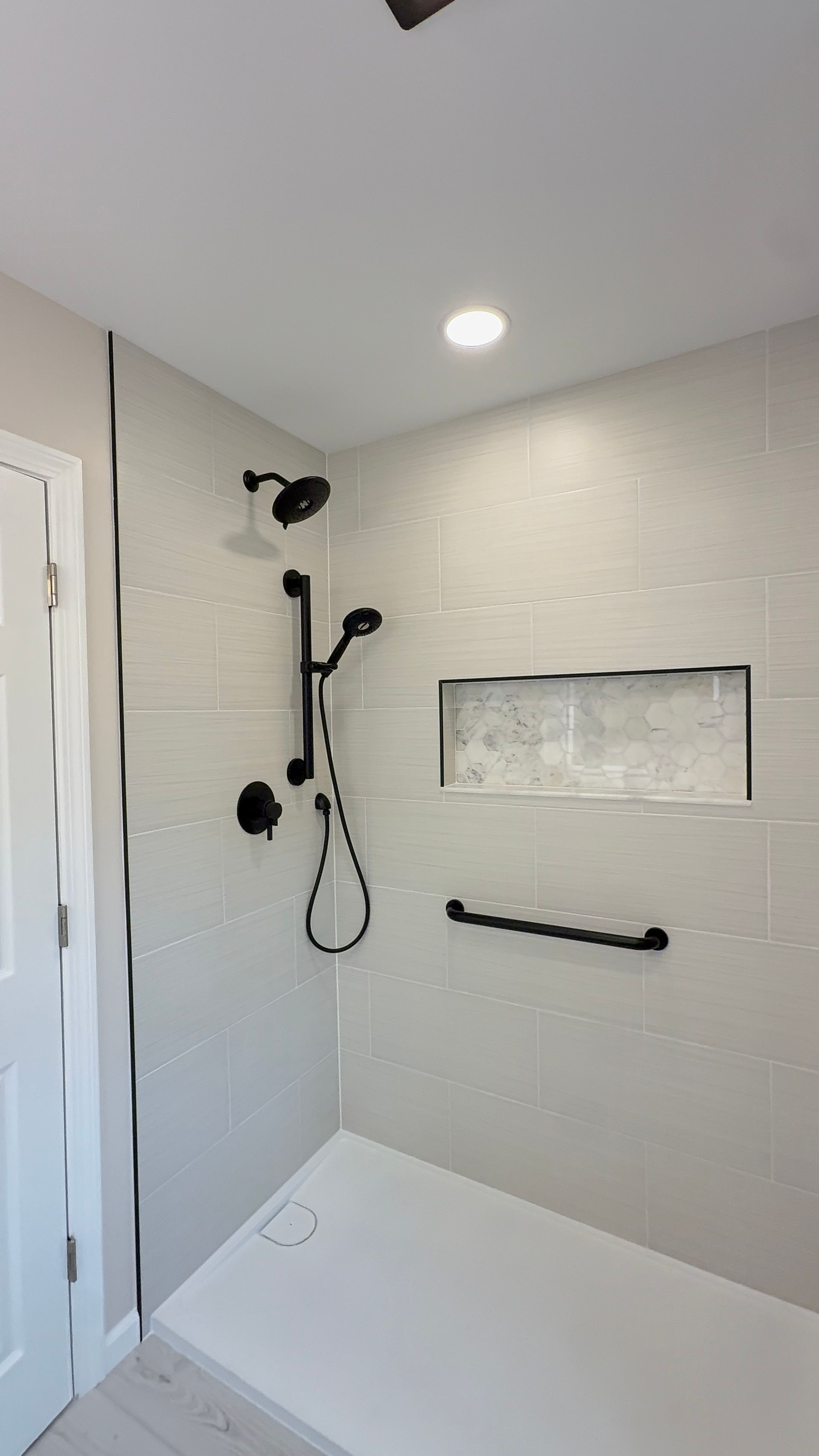 Modern shower with handheld and fixed showerheads, grab bar, and built-in bench in white tile.