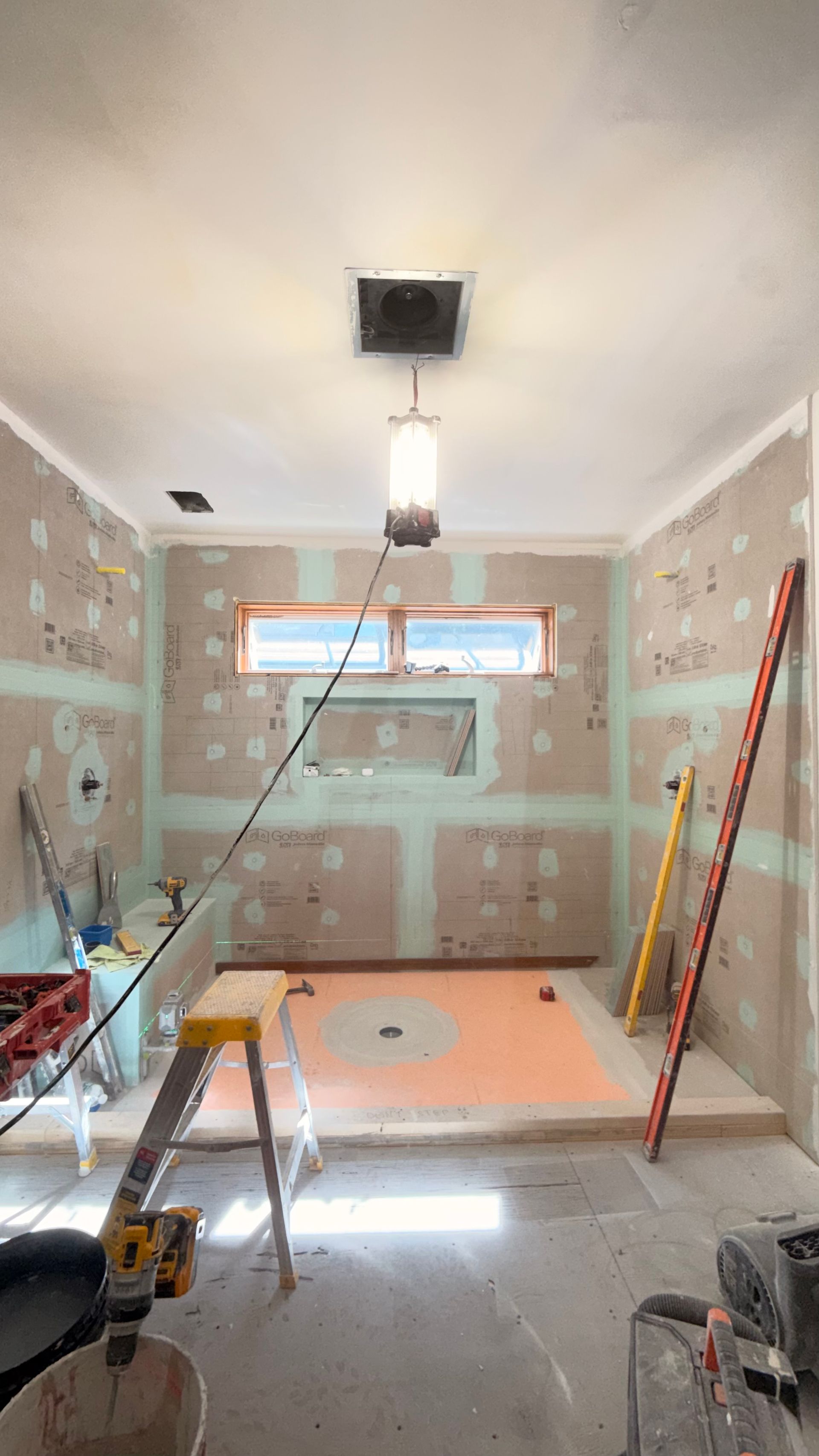 Renovation room with taped walls, exposed ceiling light, ladders, and tools on the floor.