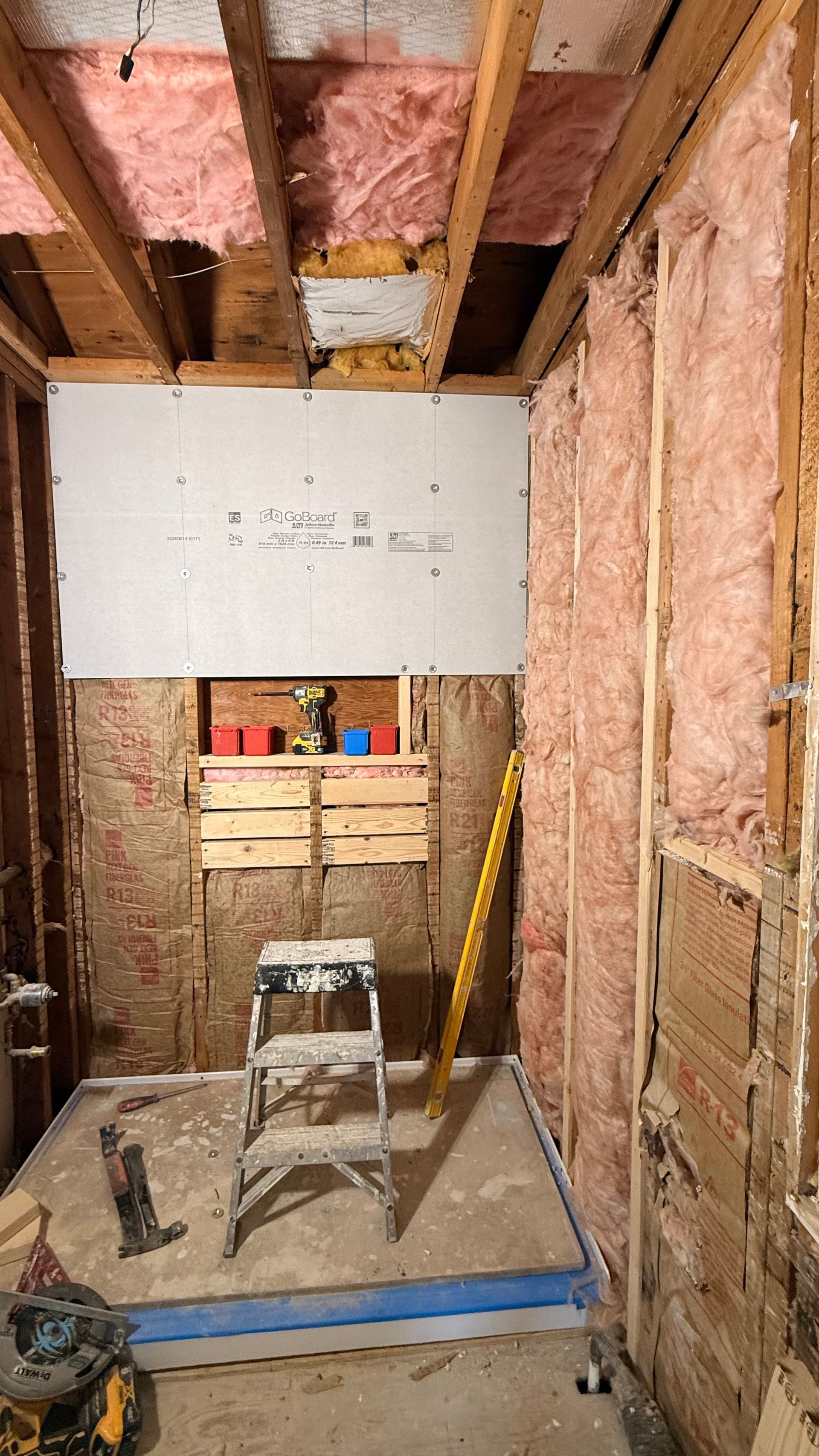Partially renovated room with exposed insulation, wooden framing, drywall, and a step ladder in the center. By First Choice Bathroom Remodeling done in Avon, CT.