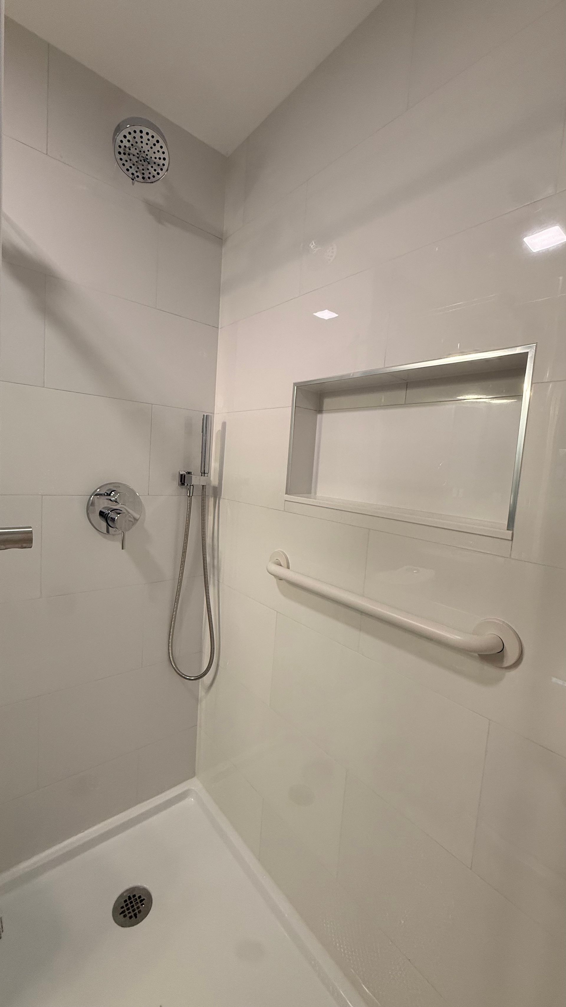 White tiled shower with grab bar, handheld showerhead, and built-in shelf niche. By First Choice Bathroom Remodeling done in Avon, CT.