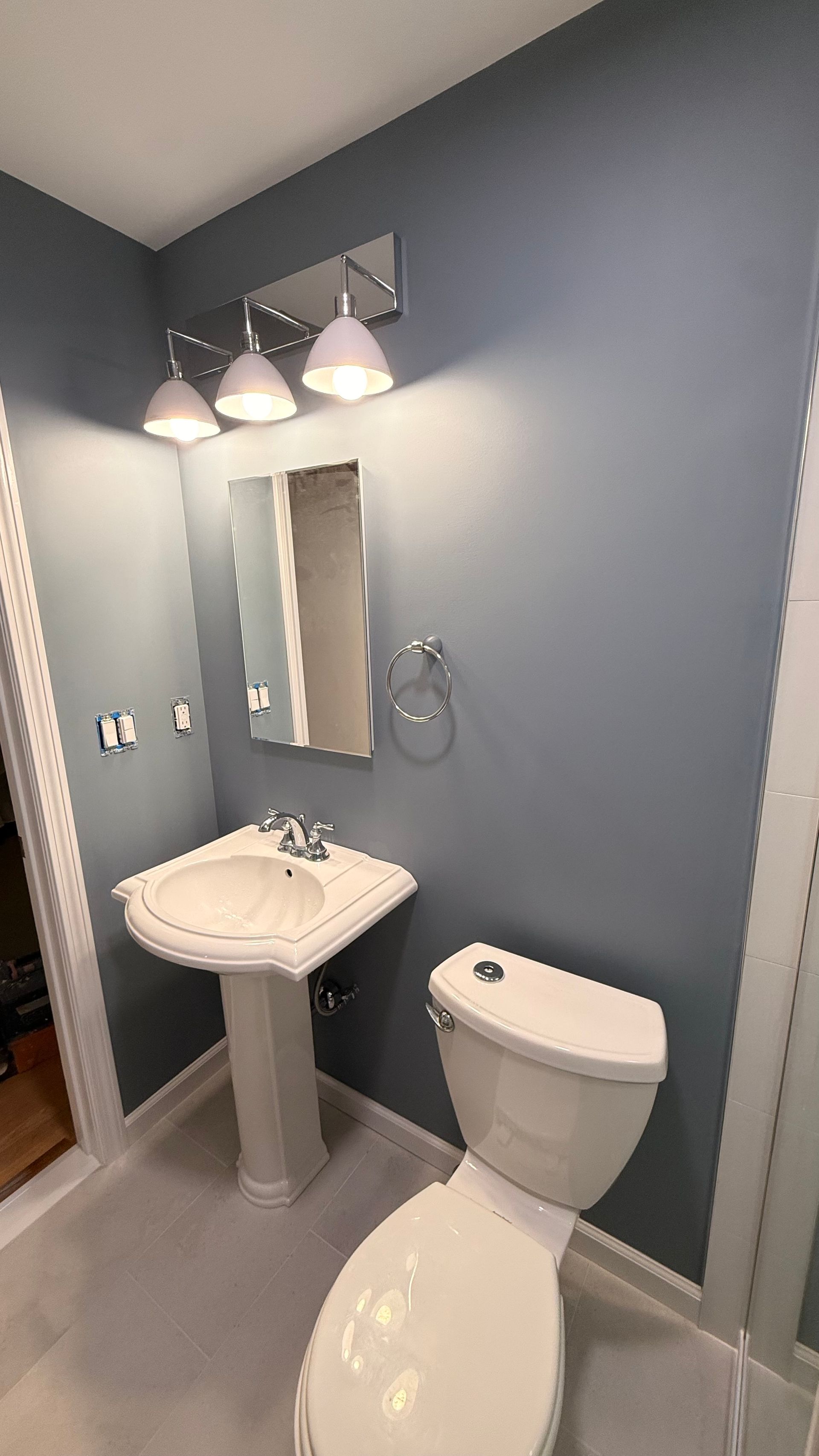 Small bathroom with blue walls, pedestal sink, toilet, mirror, and three-light vanity fixture. By First Choice Bathroom Remodeling done in Avon, CT.