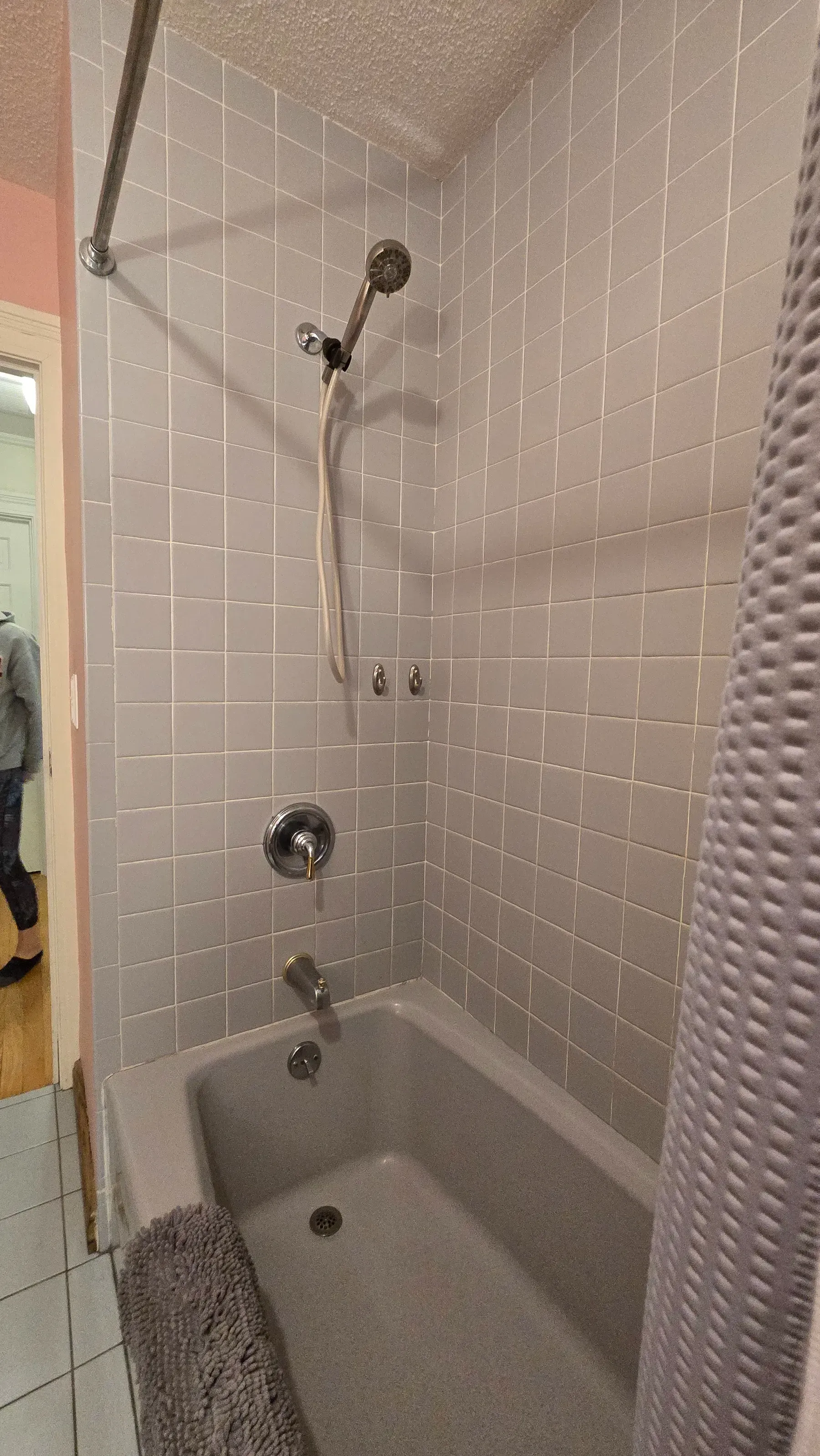 Small tiled bathroom shower with tub, chrome fixtures, and a patterned shower curtain.