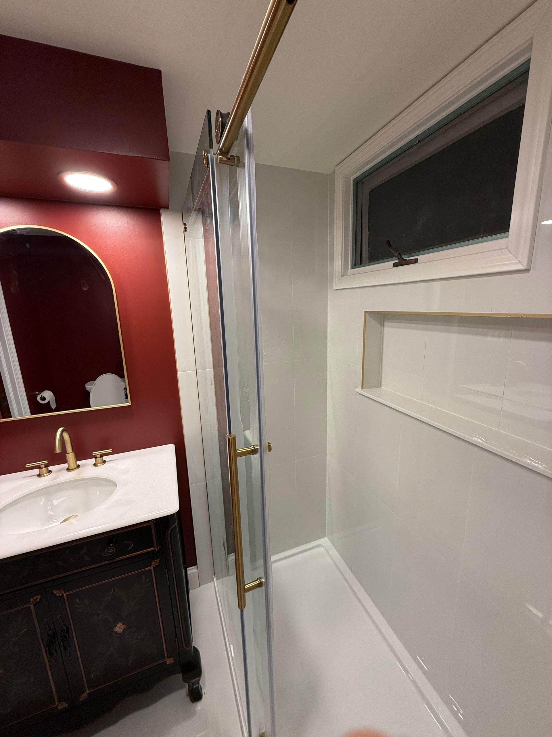 A bathroom with a sink , mirror , shower and window.