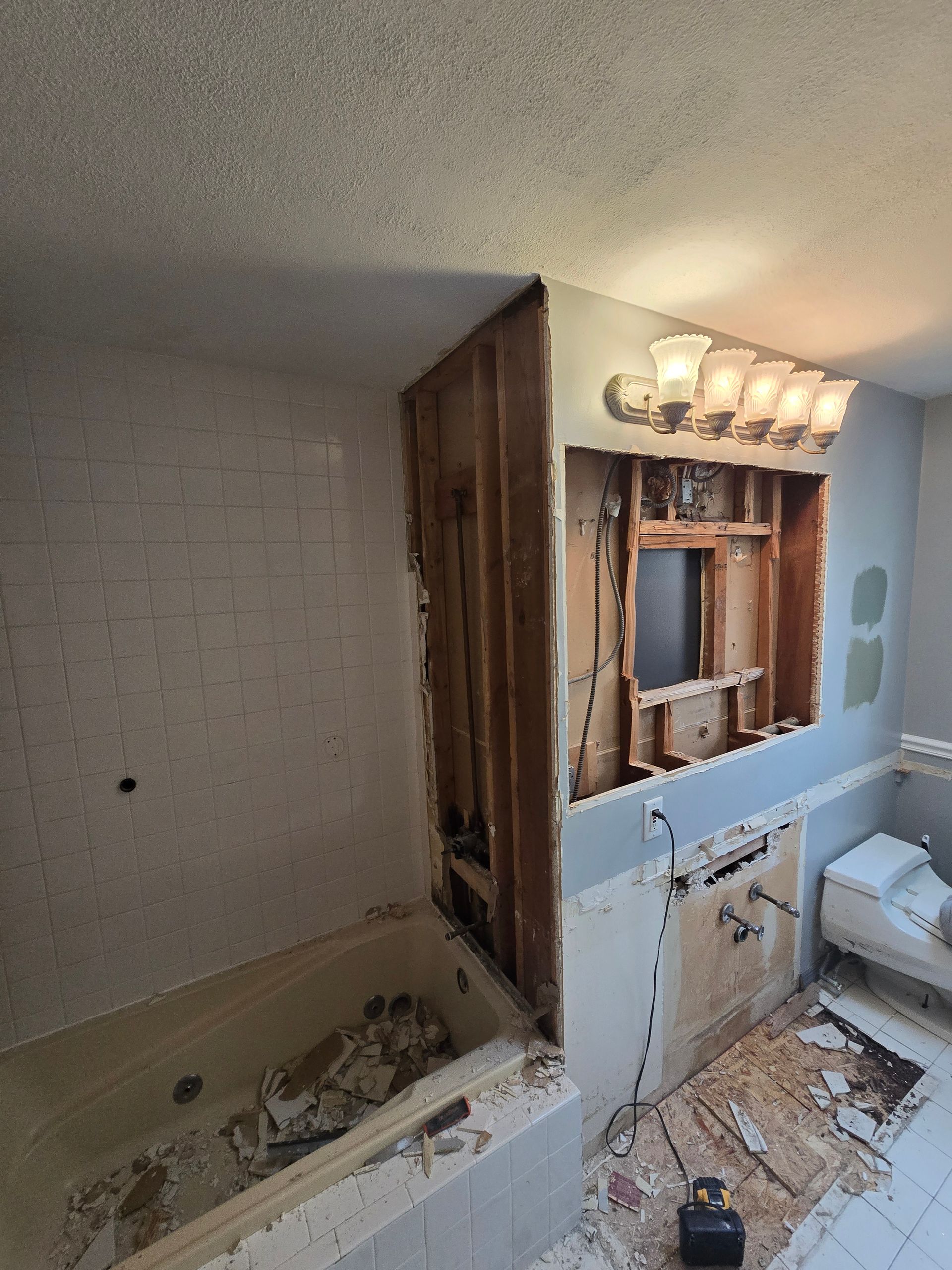 Bathroom renovation in progress: tub, framing, wall with light fixture, and toilet visible.