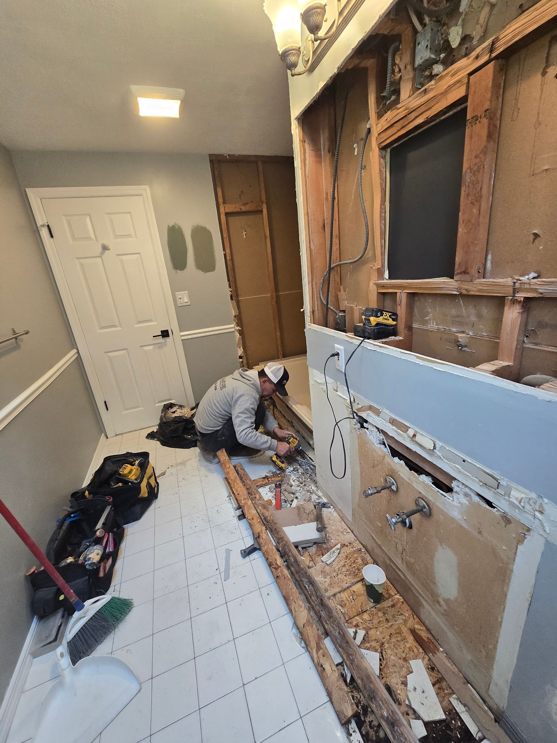 A man is kneeling on the floor in a bathroom under construction.
