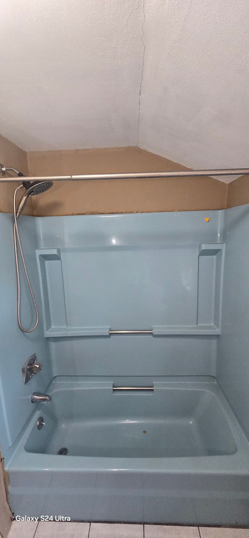 A blue bathtub with a showerhead and a curved shower curtain rod. The walls are light blue.