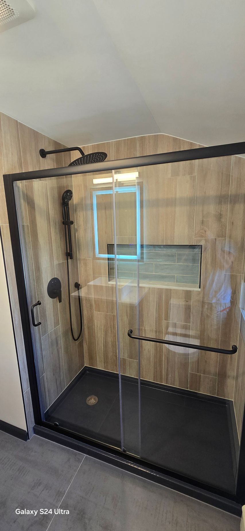 Black-framed shower with glass door, dark shower pan, and textured brown wall tiles.