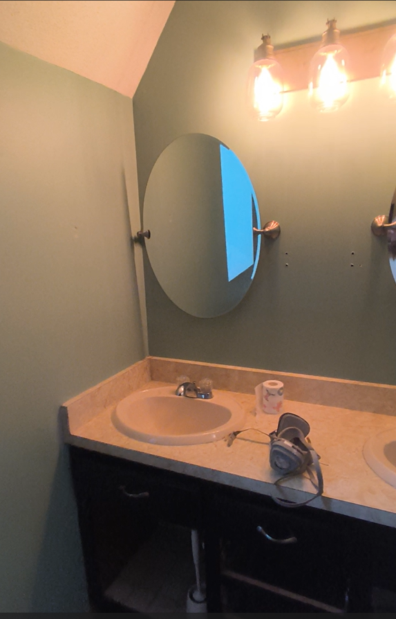 Small bathroom vanity with sink, oval mirror, beige countertop, and lights above.