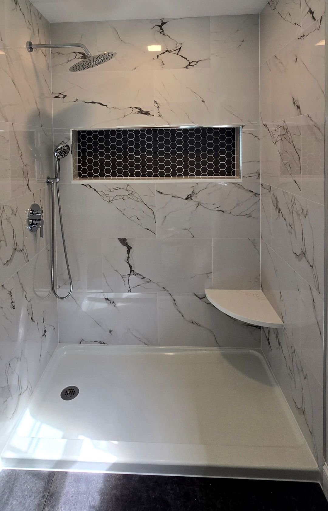 A bathroom with marble walls and a walk in shower with a seat.