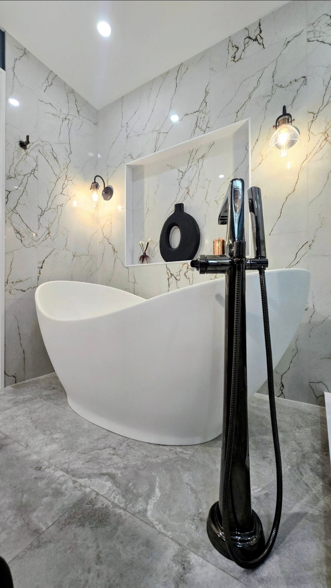 Modern bathroom remodel near Avon, CT with a white oval bathtub, marble walls, and black fixtures.