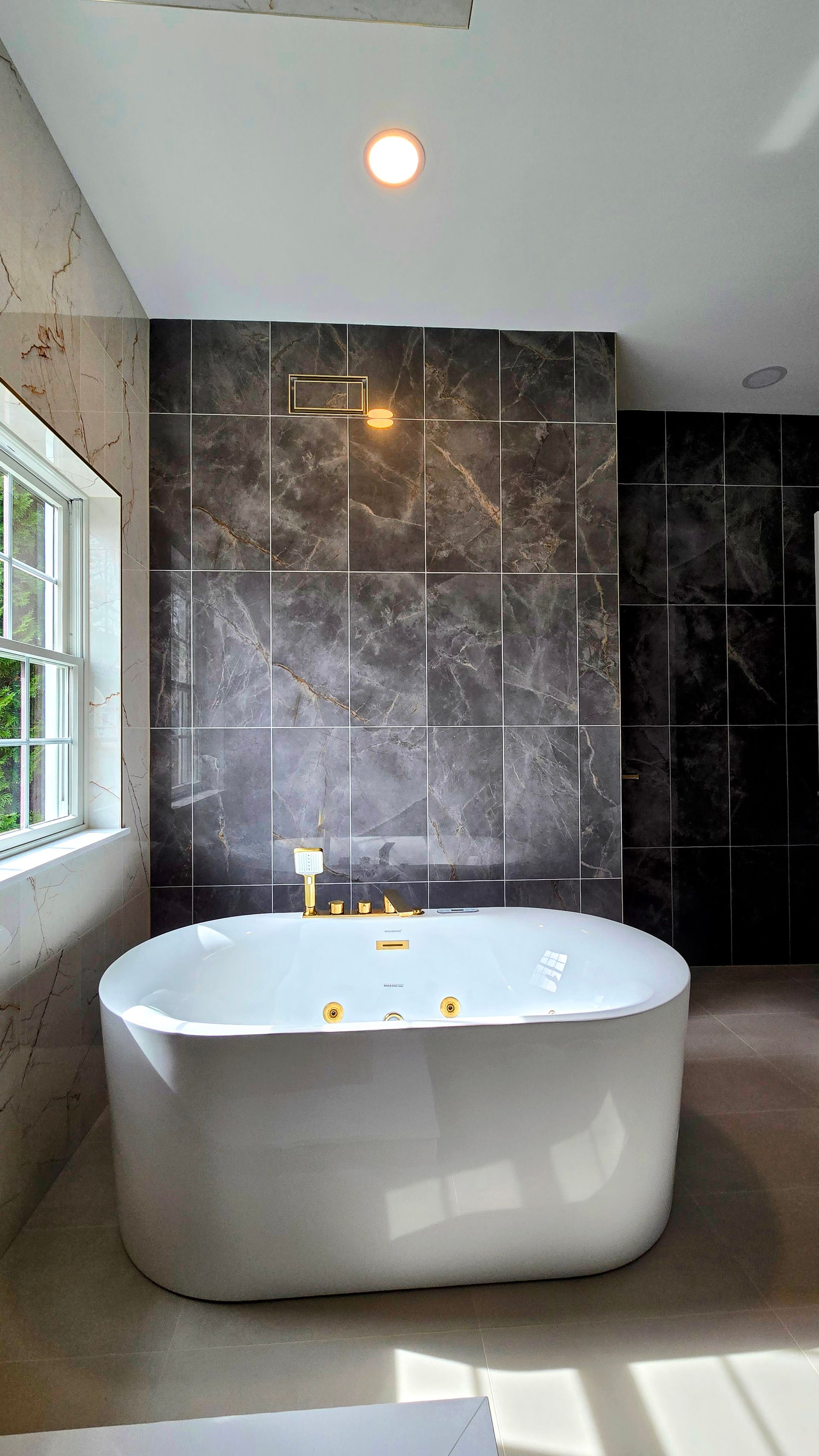 A modern white freestanding bathtub in Cromwell, CT sits in a room with a dark marble accent wall featuring metallic inlay strips.