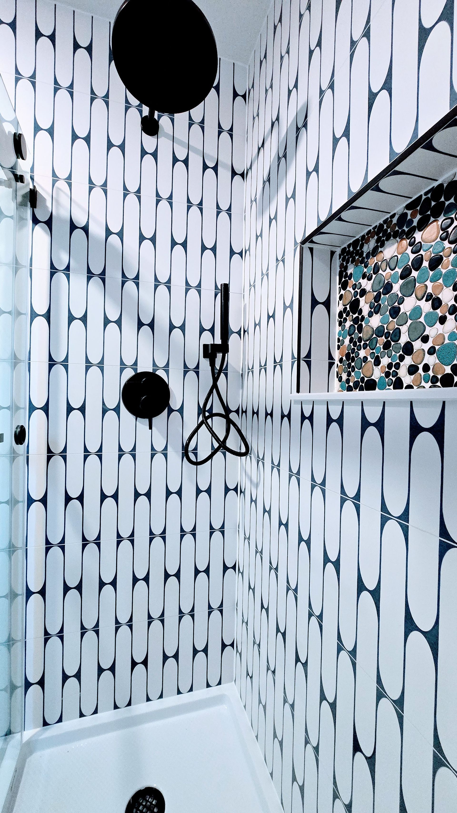 Small tiled shower corner with black-and-white patterned walls, two black wall fixtures, and a window. By First Choice Bathroom Remodeling done in Bristol, CT.