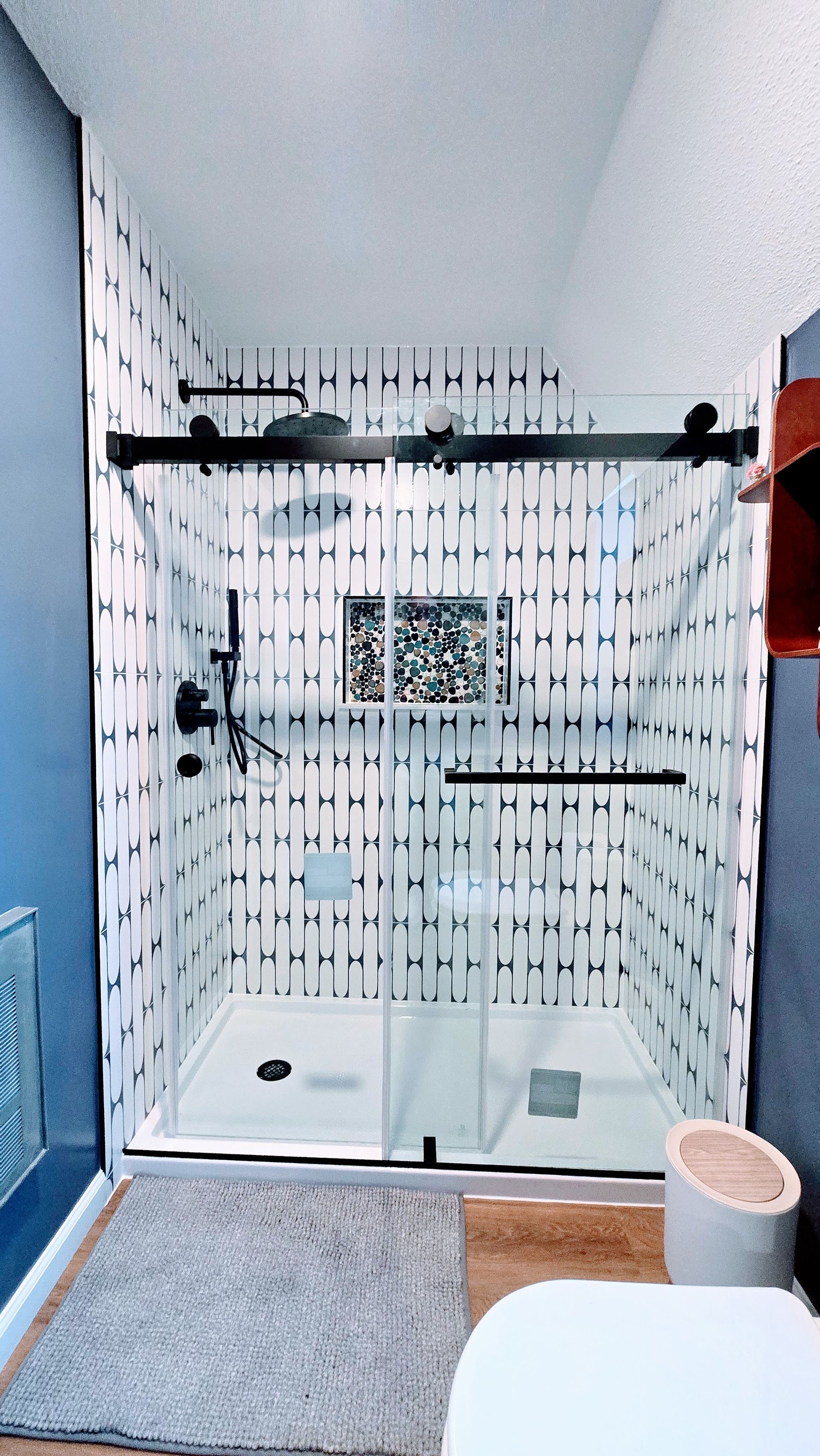 Modern bathroom with glass-enclosed shower, black fixtures, mosaic tile wall, and gray rug.  By First Choice Bathroom Remodeling done in Bristol, CT.