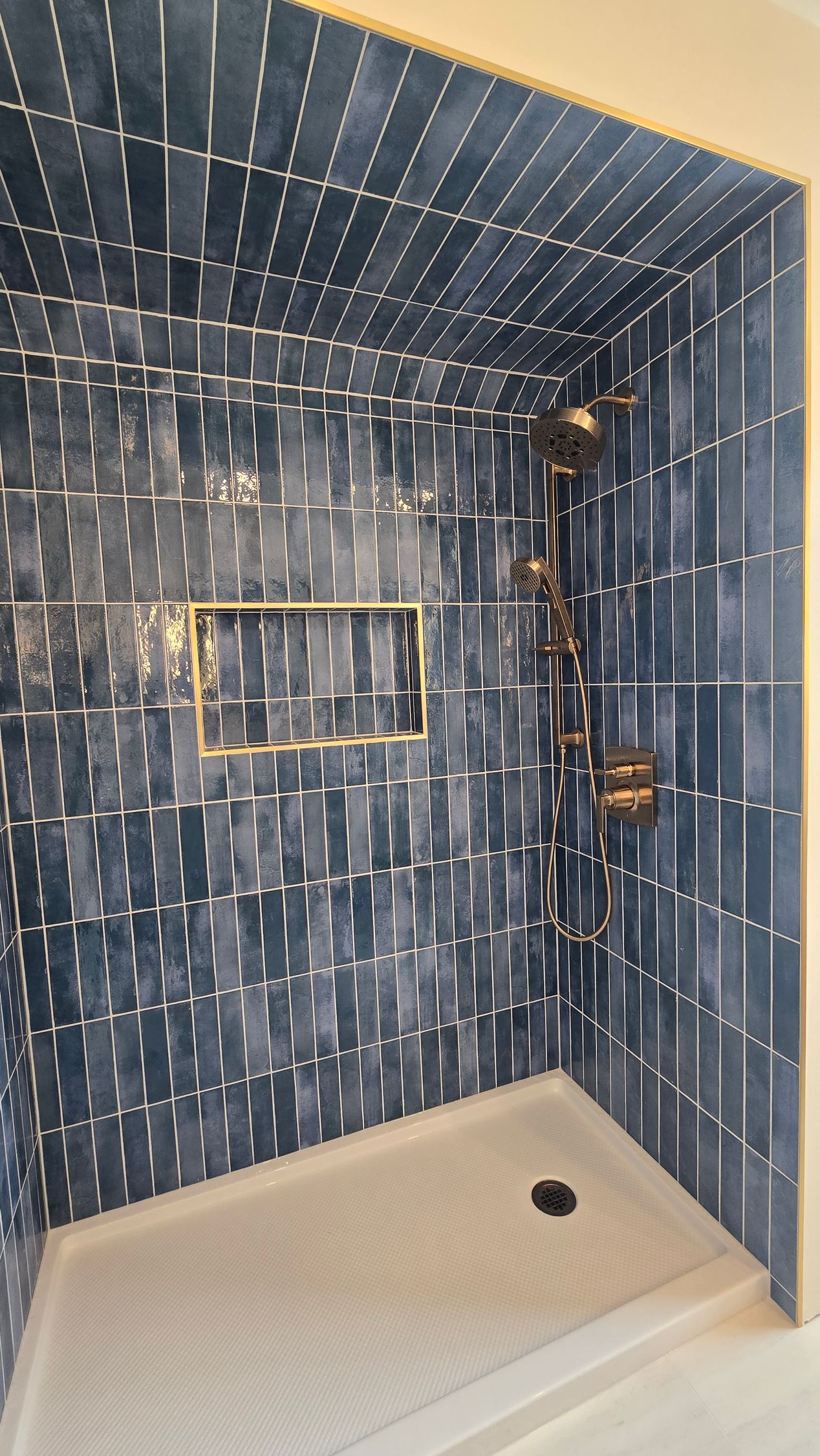 Blue tiled walk-in shower in Cromwell, CT with bronze fixtures and a recessed shelf. White shower base.
