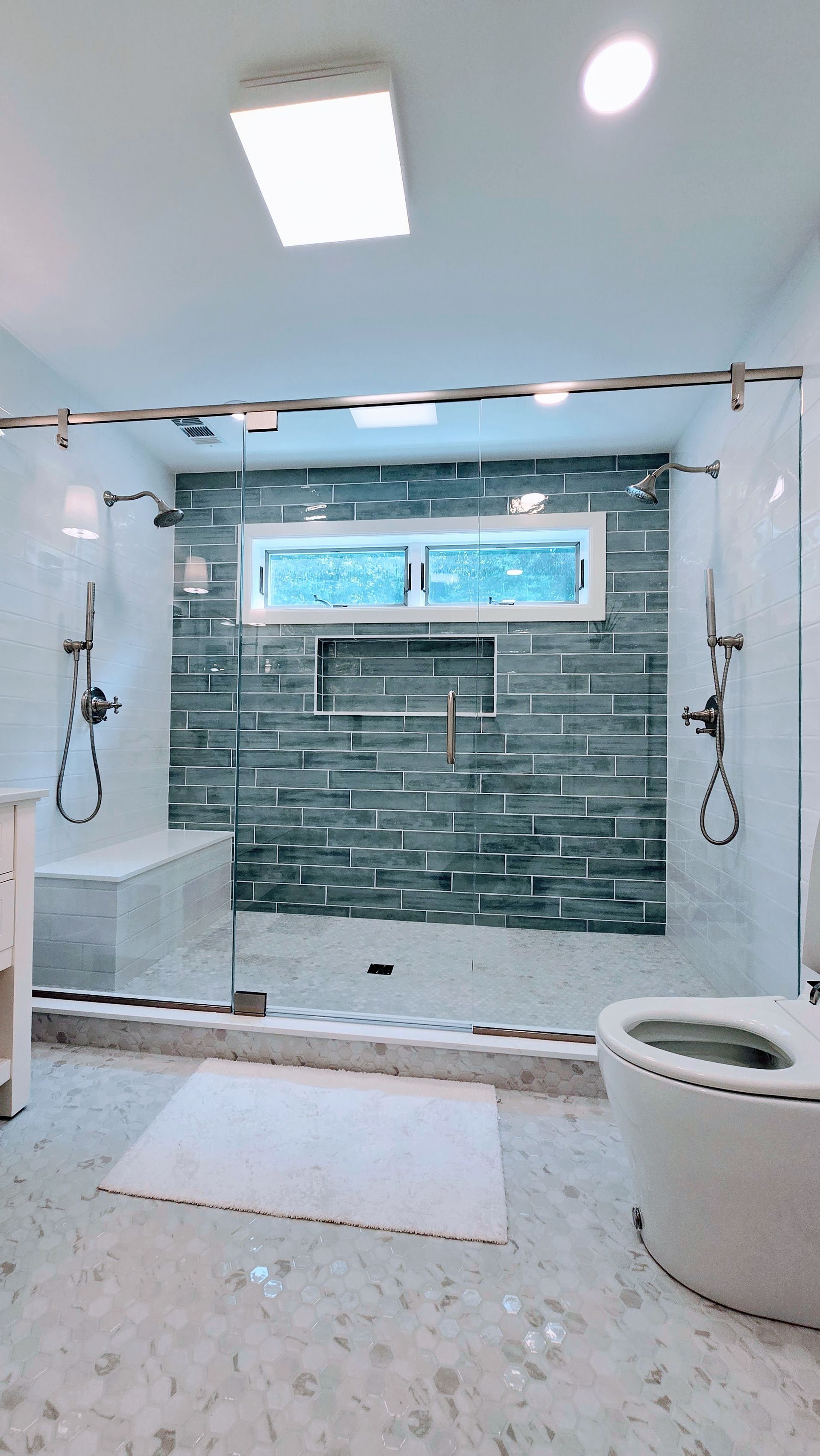 Modern bathroom in Rocky Hill, CT with walk-in shower, gray tile accent wall, window, and white vanity on the right