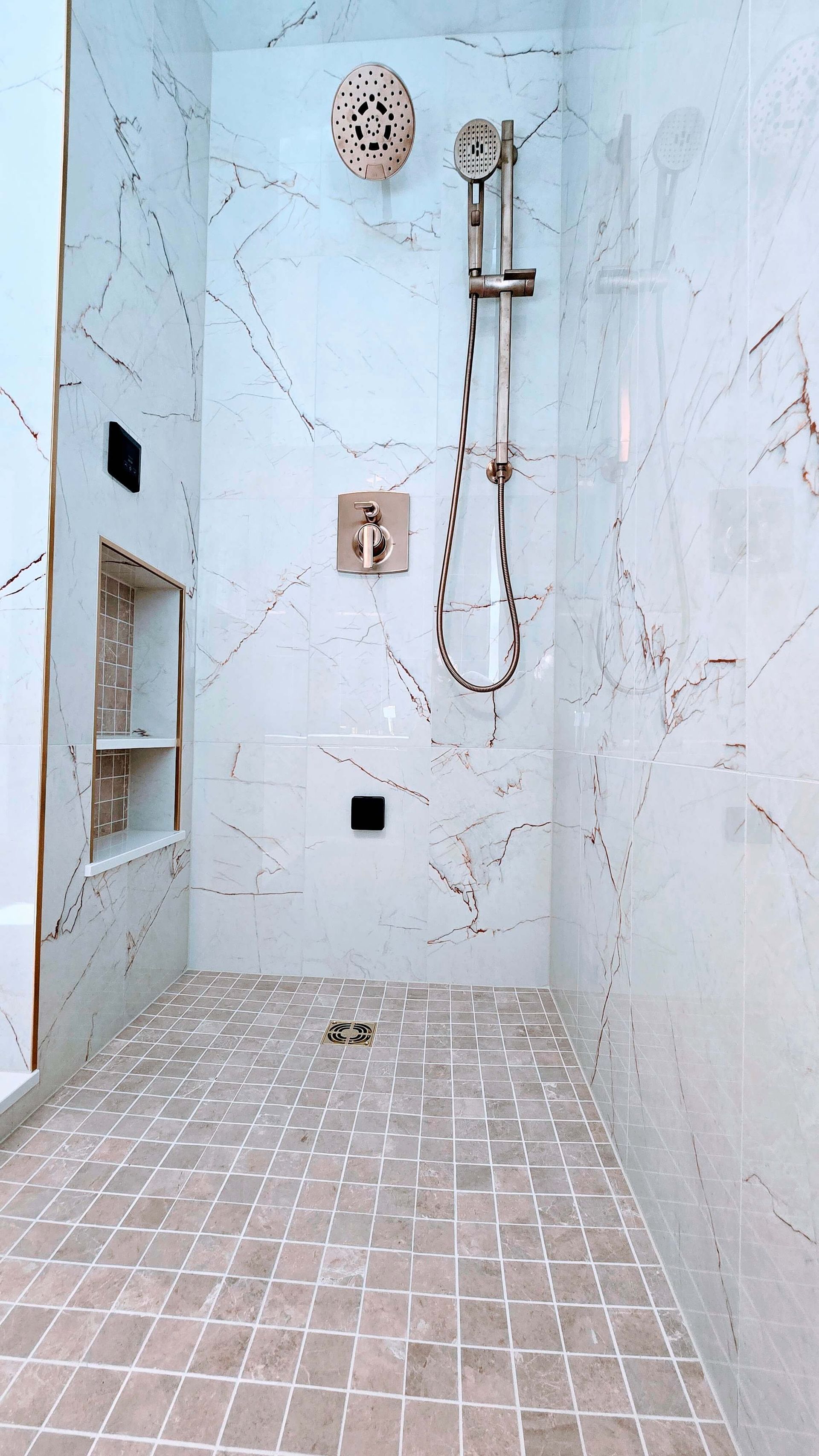 Modern shower area with white marble-look tiles, mosaic floor, and wall-mounted shower fixtures