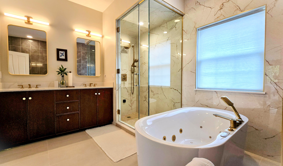 Elegant bathroom with glass shower, dark vanity, beige tile, and a white soaking tub near the window