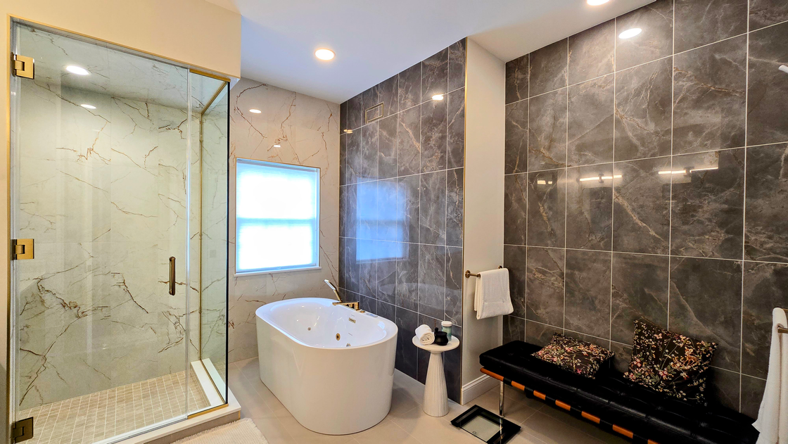Modern bathroom with glass shower, freestanding tub, dark tile walls, and a fireplace.