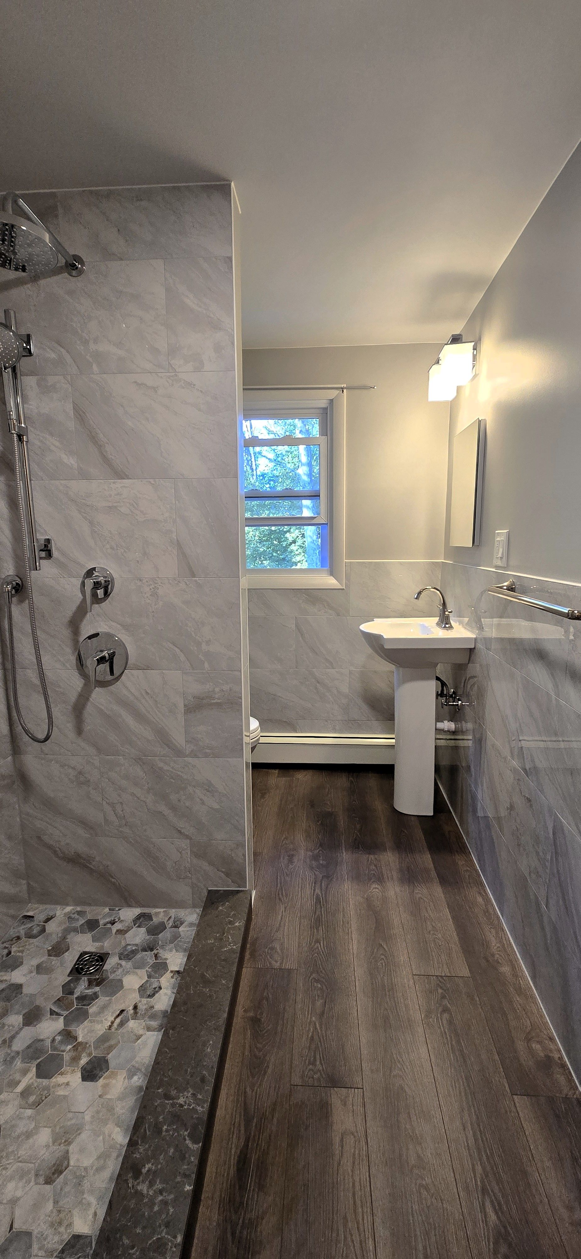 Bathroom with blue walls, dark vanity, and marble-patterned floor. A window and a large mirror are present.