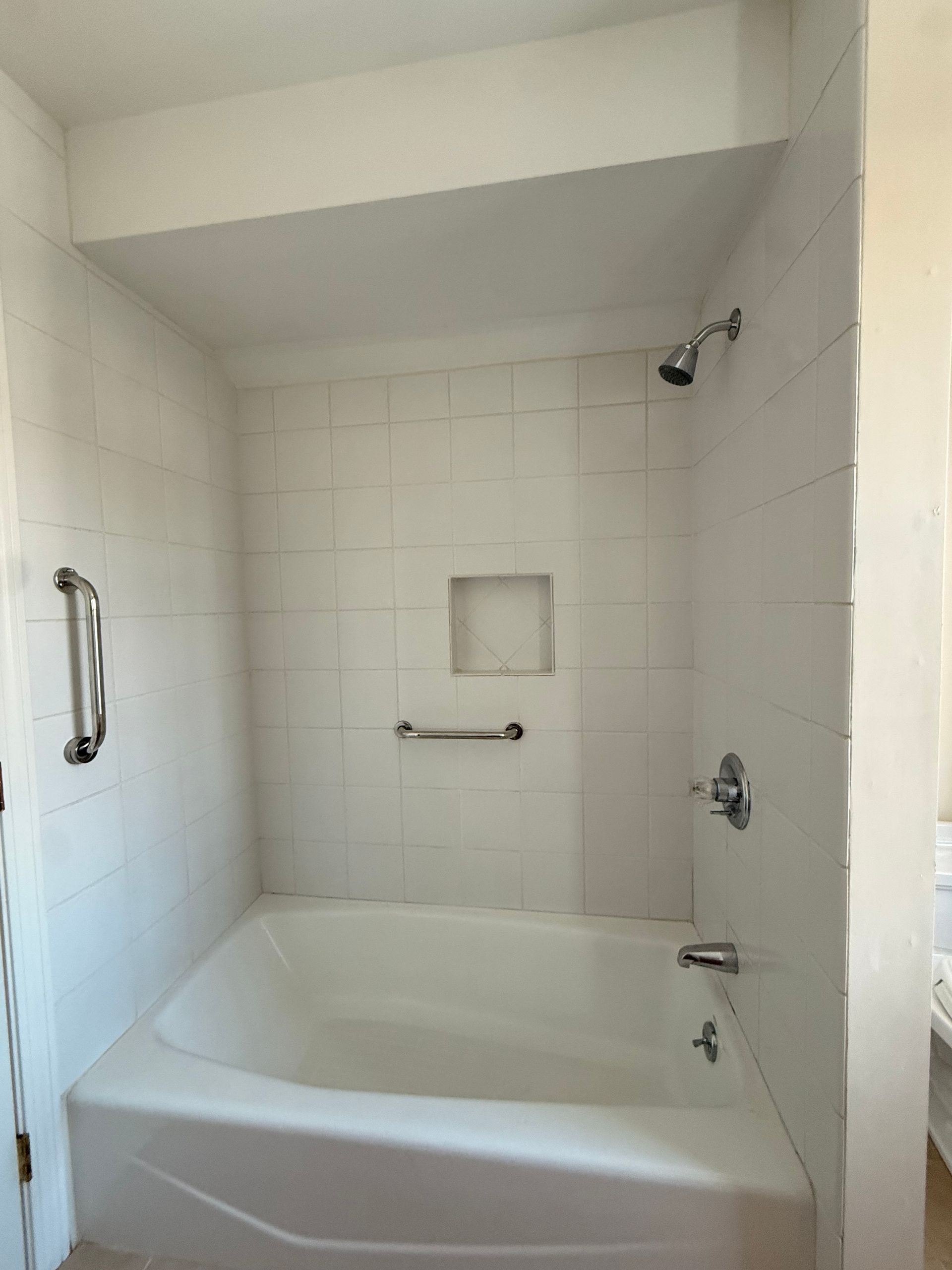 A view of a bathroom showing a toilet in a small alcove next to a bathtub with white tile walls.