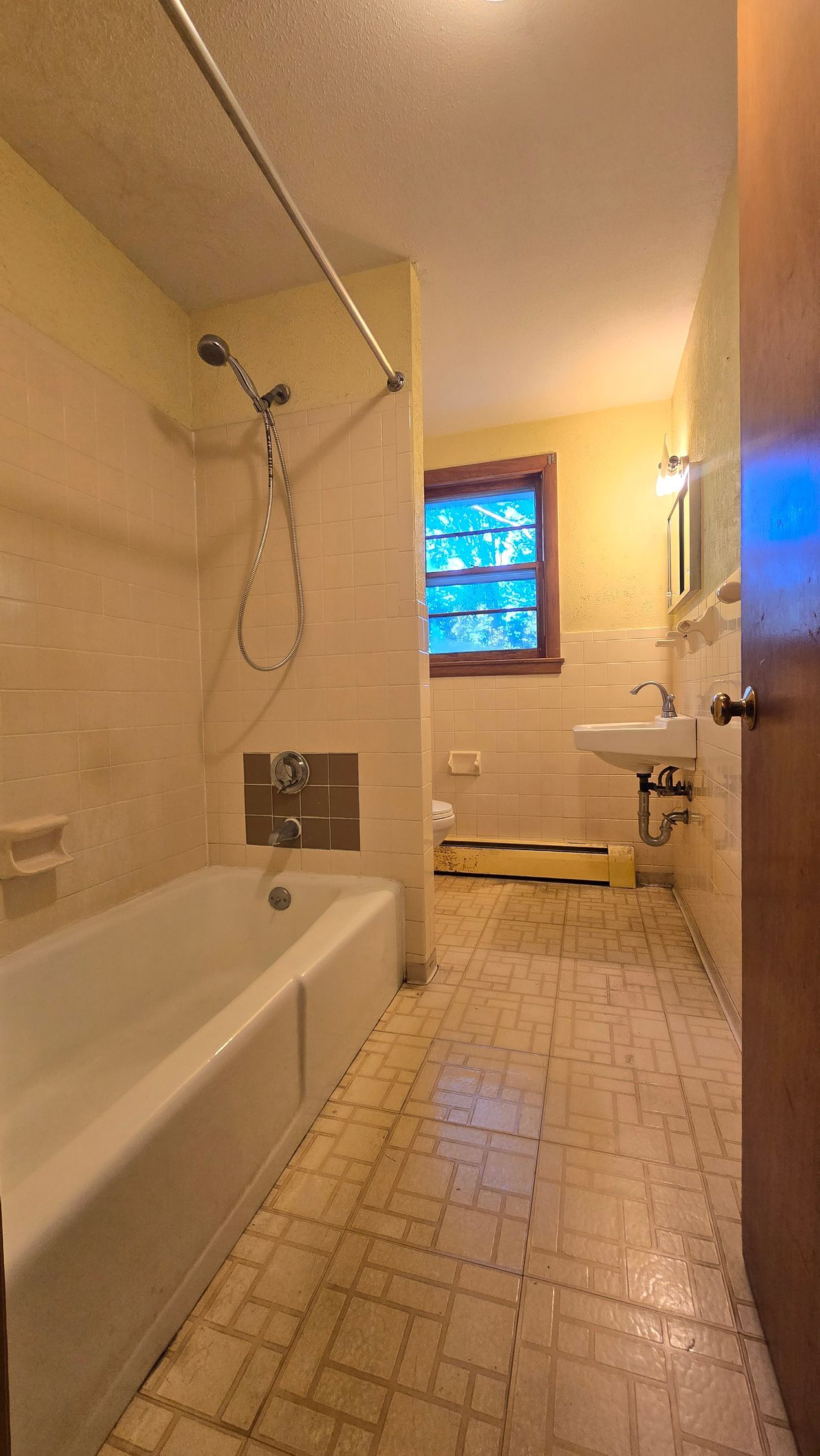 Southington bathroom with a bathtub, sink, and window. Yellow tile walls and floor, shower curtain rod.