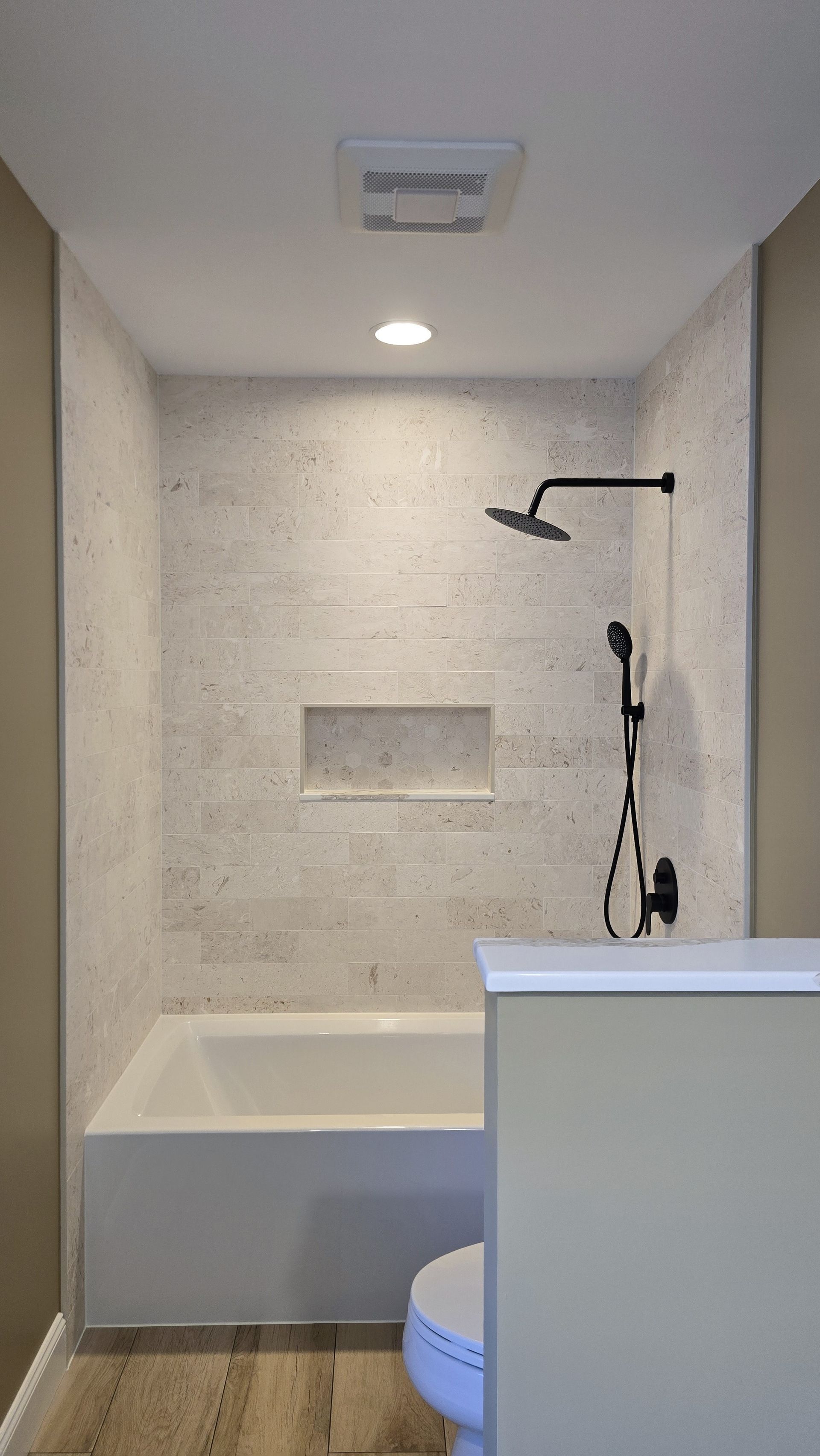 Bristol Bathroom with white bathtub, stone tile shower, black shower fixtures, recessed shelf.