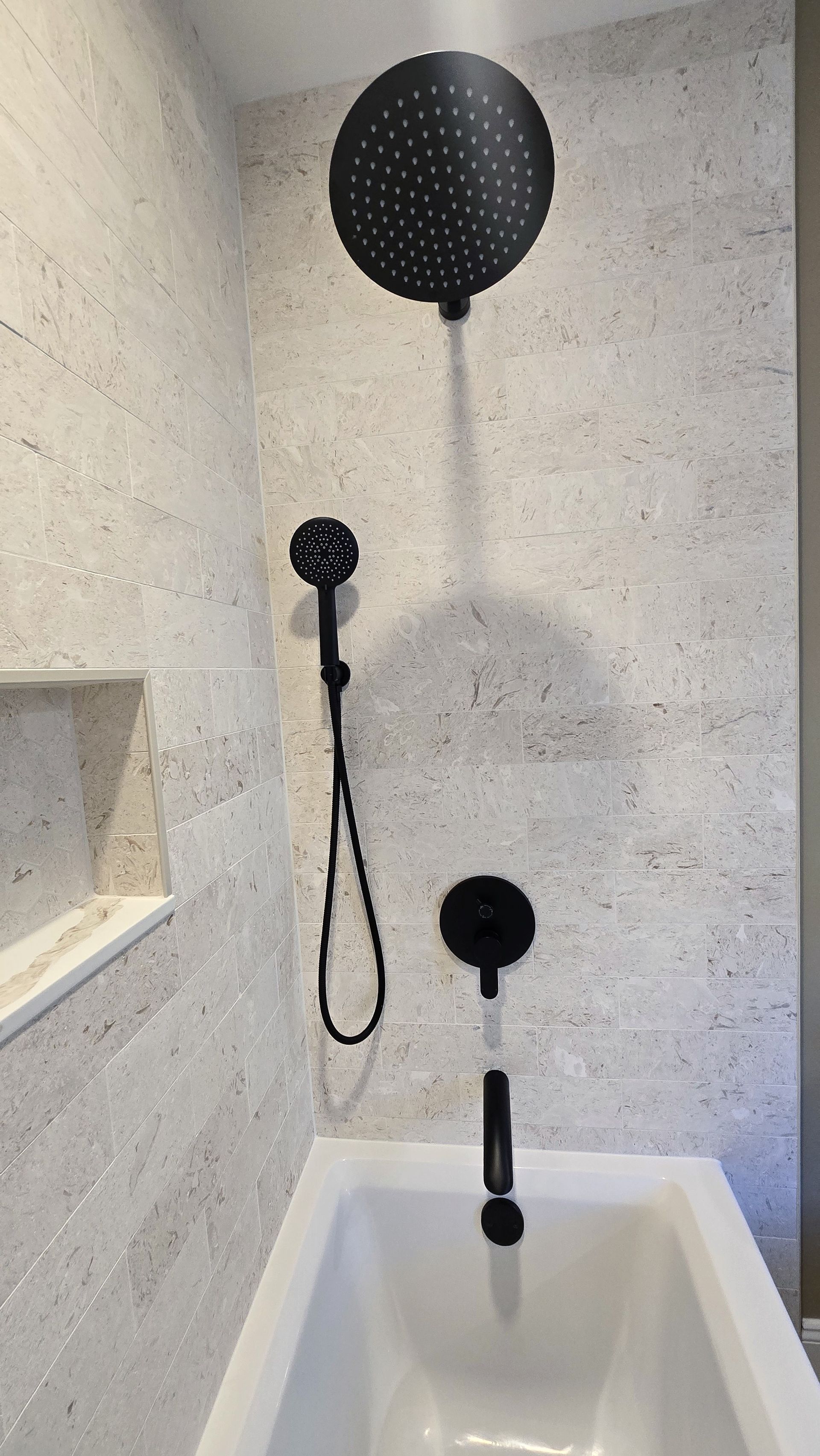 Luxurious walk-in shower renovation in Wolcott, CT with herringbone tile, bronze fixtures, glass enclosure, and a built-in shelf.