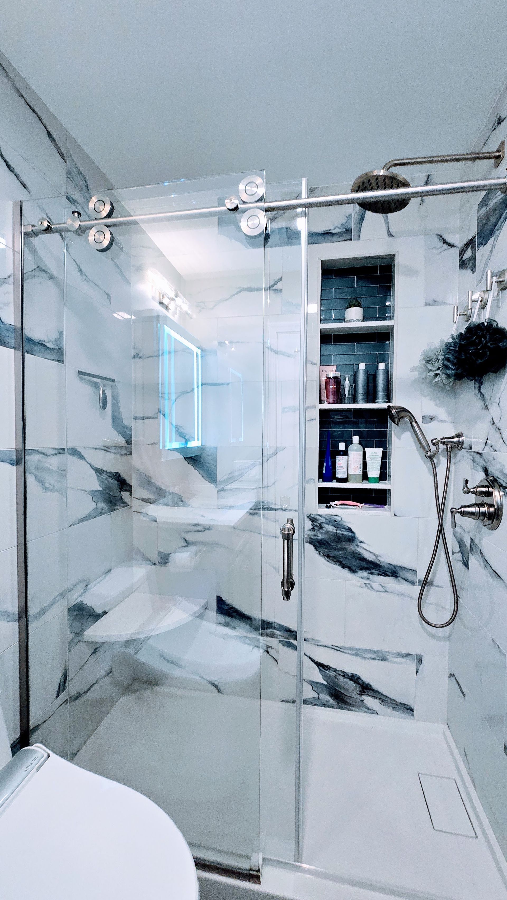 Bathroom with blue walls, dark vanity, and marble-patterned floor. A window and a large mirror are present.