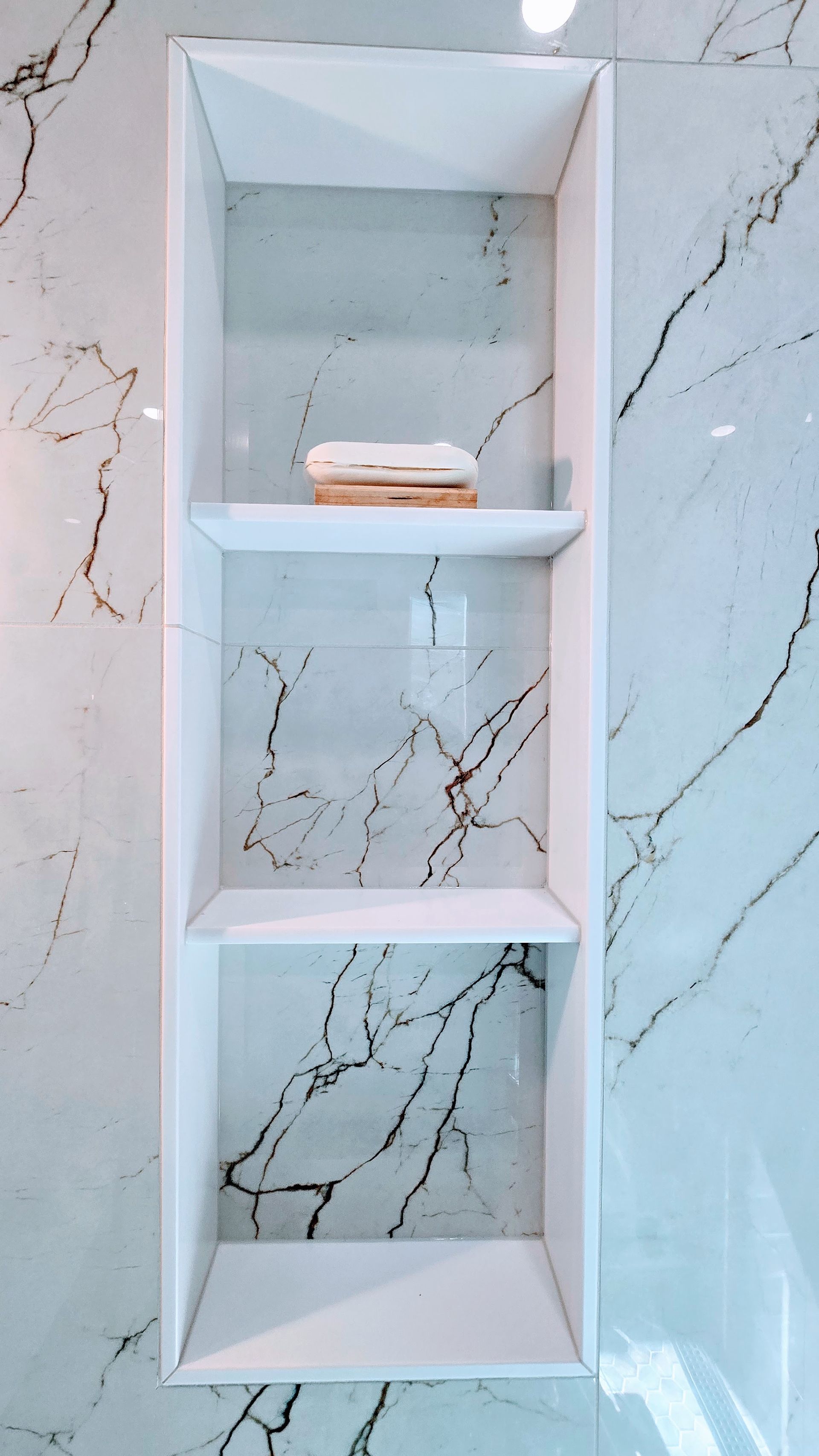 White built-in shelves in a marble-look wall; one shelf holds a beige and brown bar of soap.