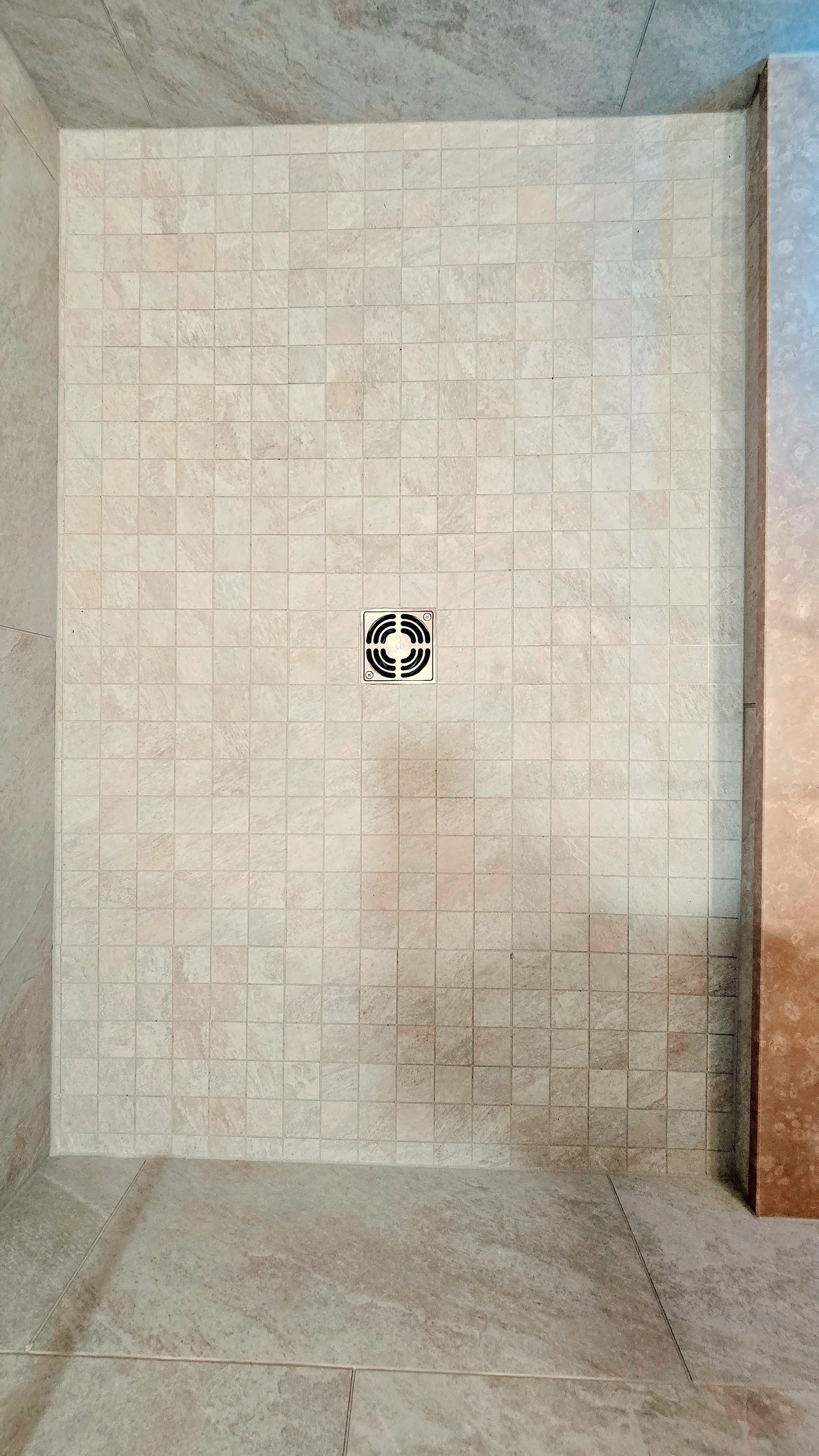 A light-colored stone-tiled shower wall with a small, square, decorative patterned tile in the center.