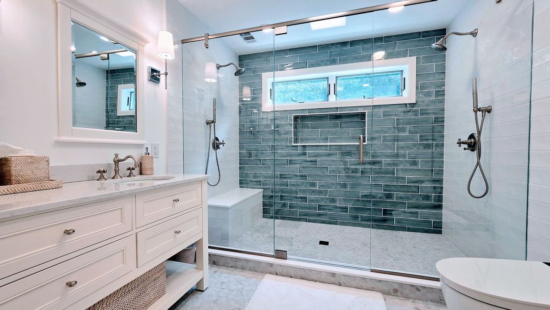 Bright bathroom with walk-in shower, blue tile accent wall, white vanity, and window above the shower.