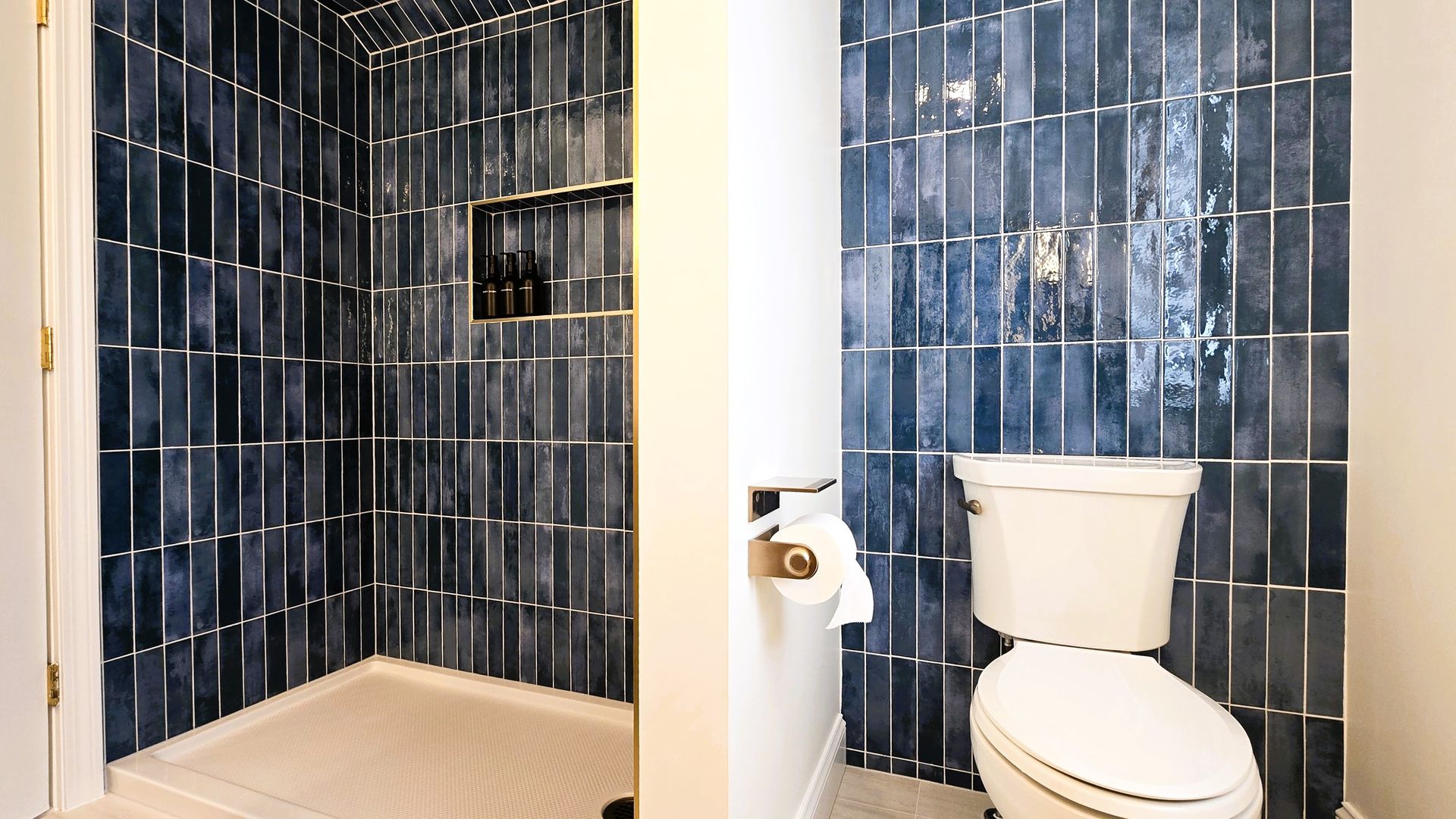 A side-by-side view showing a walk-in shower and a toilet, both featuring vertical, glossy, deep-blue subway tile walls.