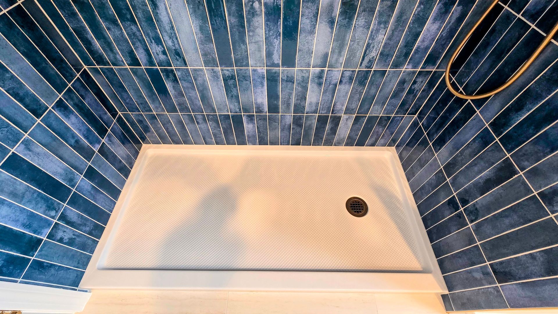 Blue tiled shower with a beige bench seat and a small drain hole.