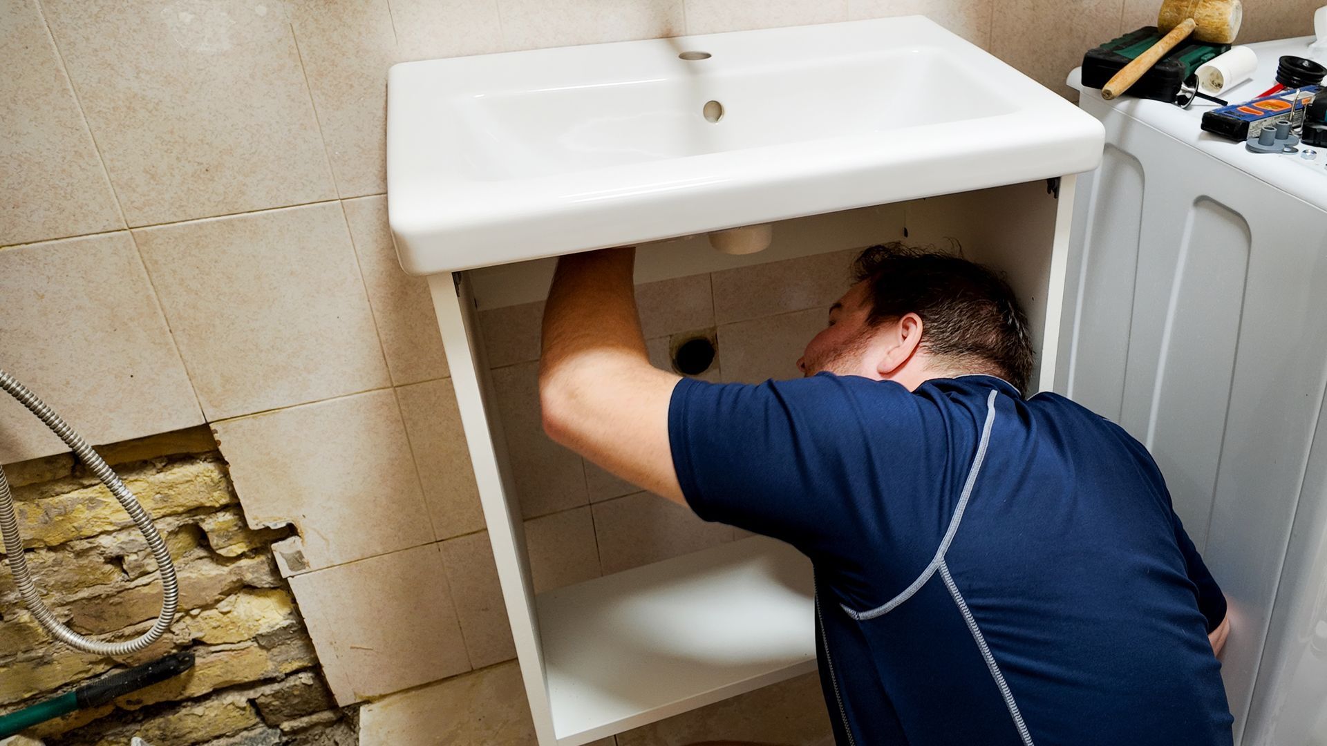 A plumber repairs a bathroom sink, illustrating plumbing maintenance challenges