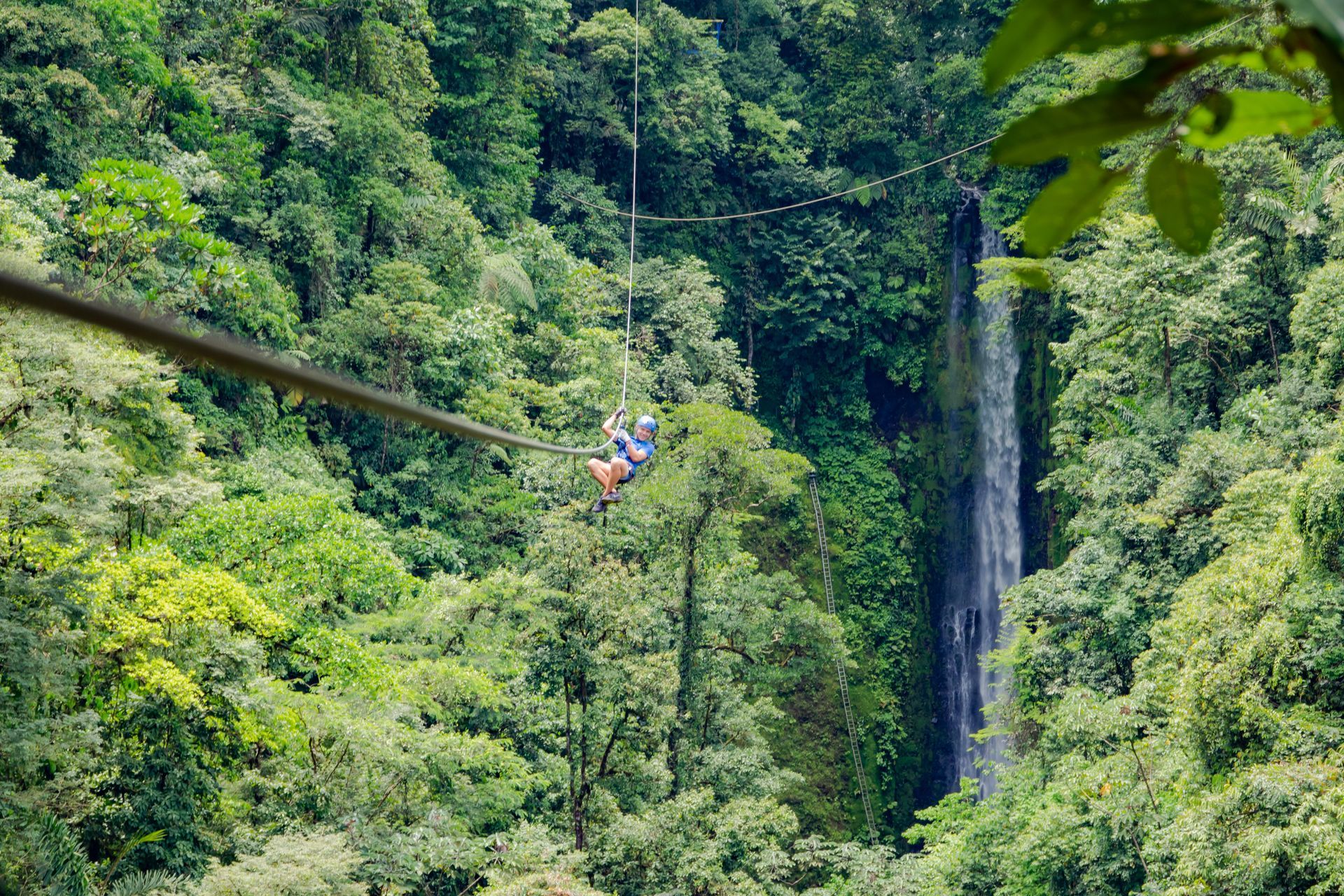 a person is riding a zip line over a waterfall in the jungle .