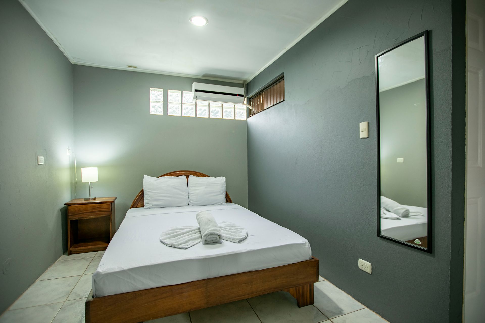 a bedroom with a bed , nightstand , mirror and air conditioner .