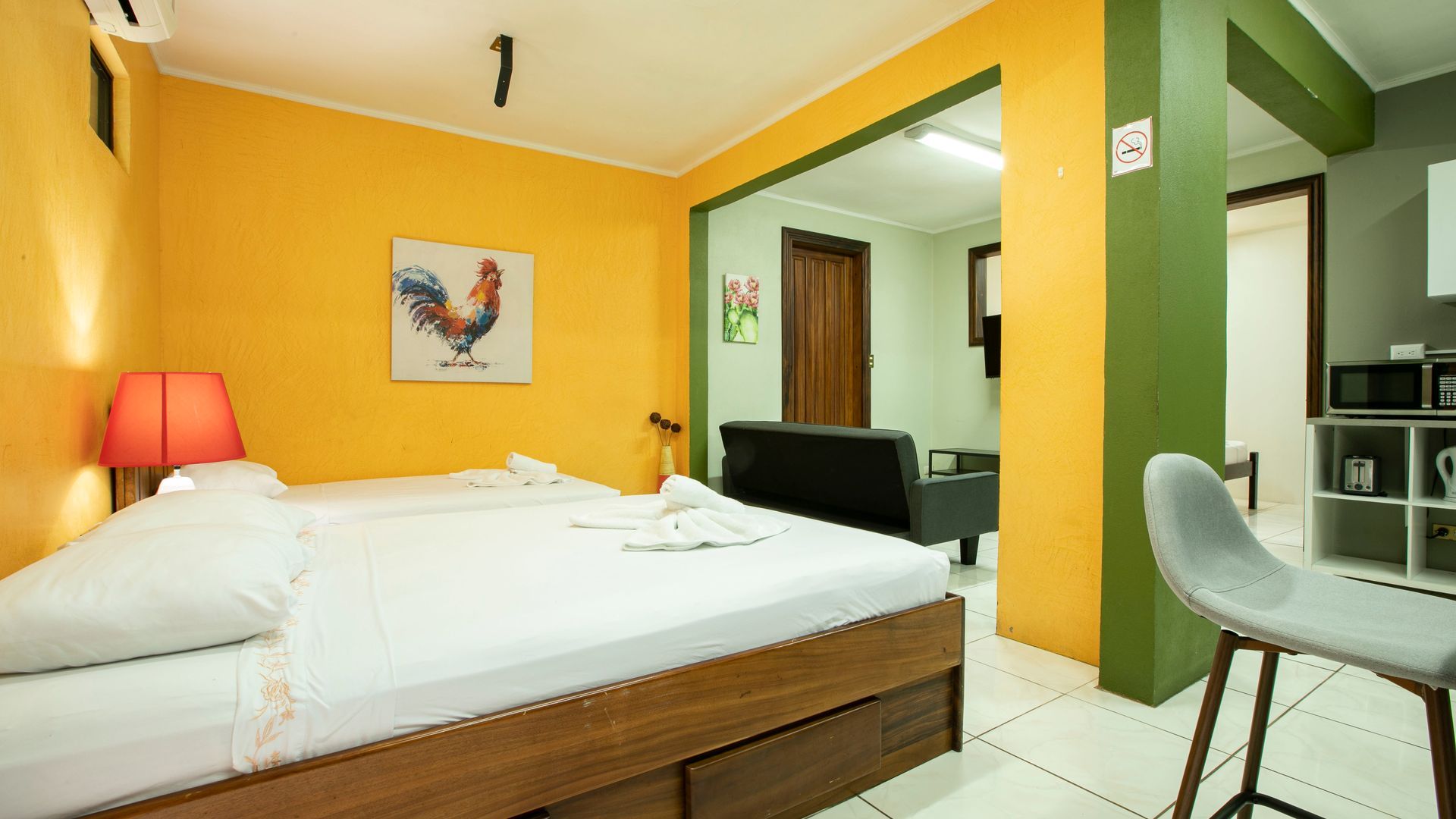 a bedroom with a bed , chair , lamp and a painting of a rooster on the wall .