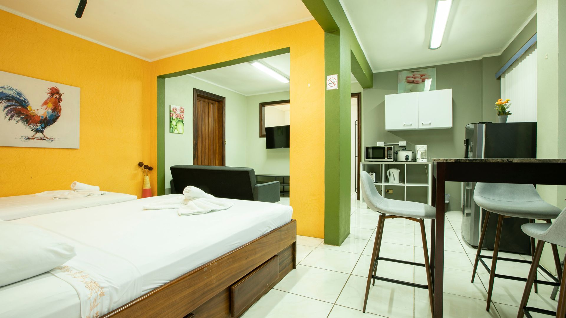 a bedroom with a bed , table , chairs and a painting of a rooster on the wall .