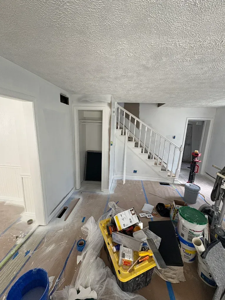 An indoor view of a room undergoing renovation, showing a white staircase, a small closet, and construction supplies.
