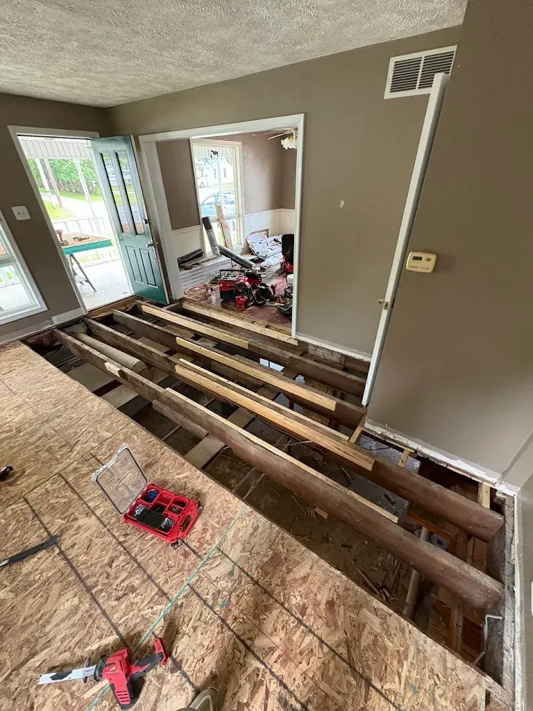 A room renovation showing exposed floor joists, a subfloor, and a doorway leading to another work area.