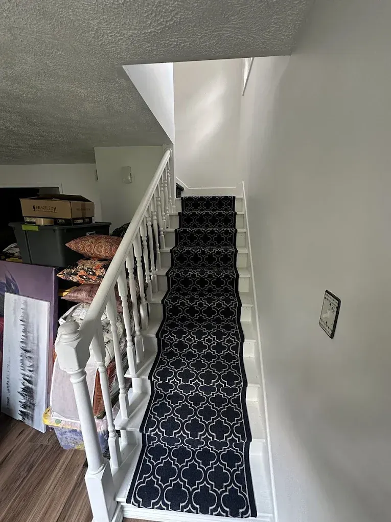 A staircase with a white railing and banister, featuring a dark blue runner rug with a white geometric pattern.
