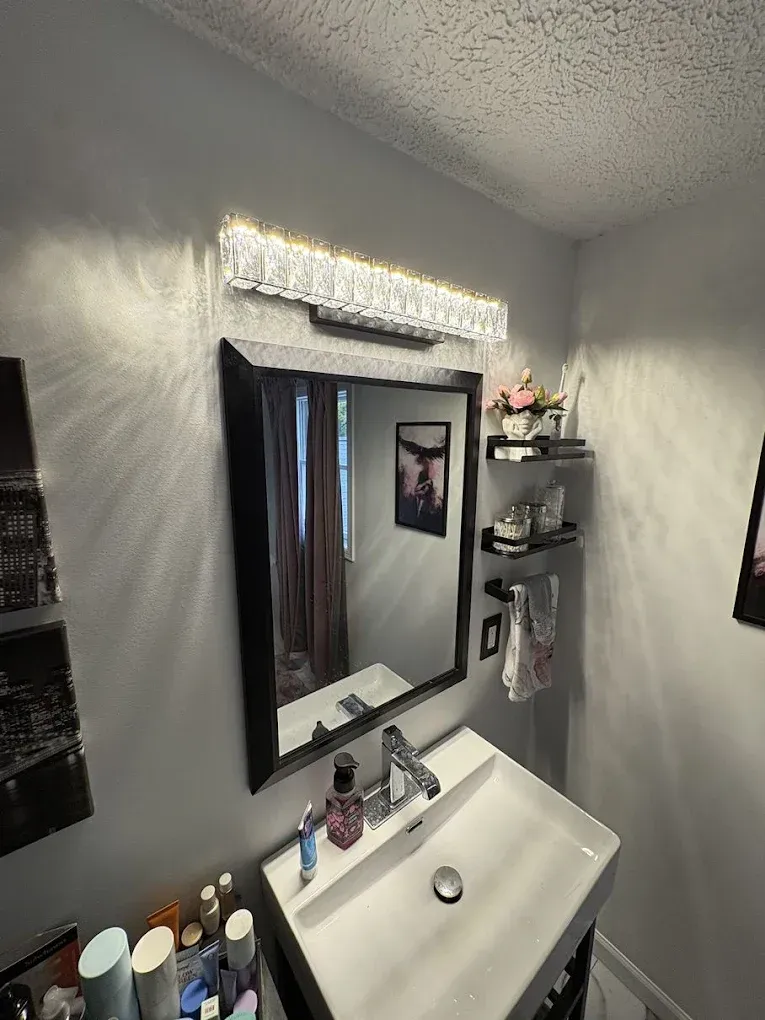 A modern bathroom vanity featuring a rectangular mirror, a bright crystal light fixture, and a white sink.