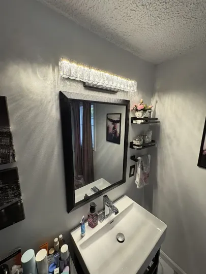 A modern bathroom vanity featuring a rectangular mirror, a bright crystal light fixture, and a white sink.