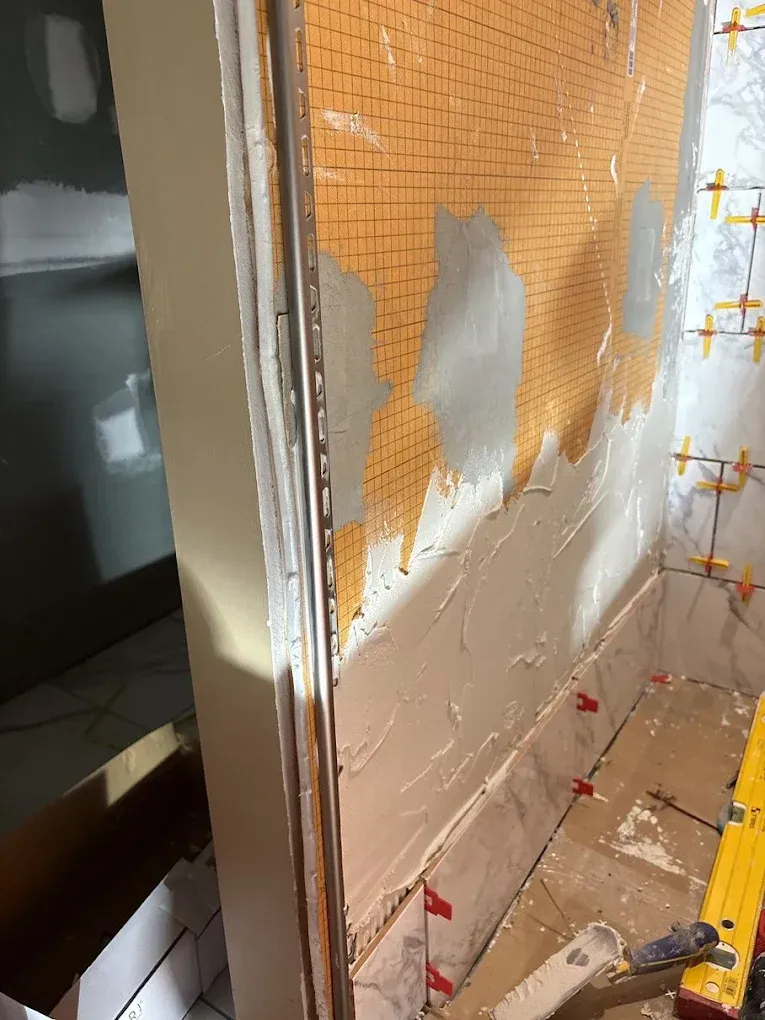 A partially tiled shower wall with orange waterproof membrane partially covered by thin-set mortar and installed tiles.