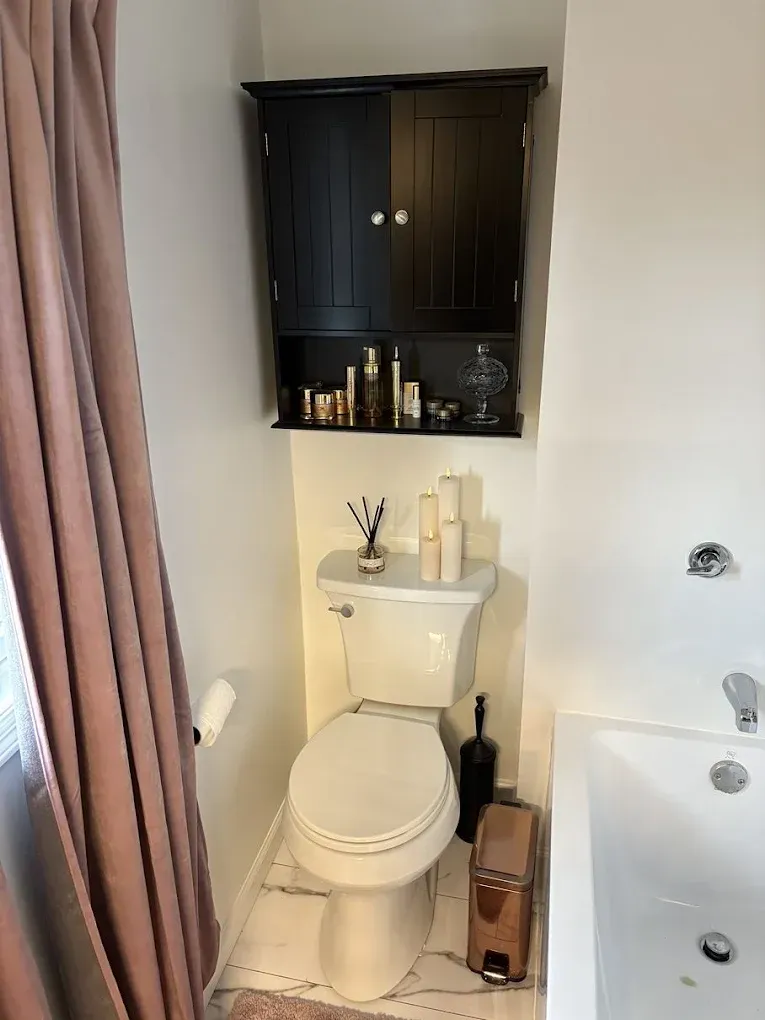 A bathroom showing a white toilet, a brown wall cabinet with shelves, a pink shower curtain, and a white bathtub.