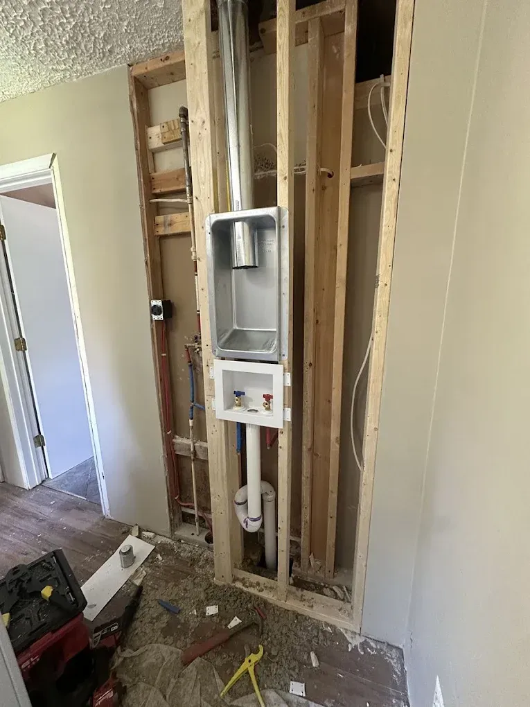 Exposed laundry wall in a home with a dryer vent box, water supply valves, and drain pipe installed between wall studs.