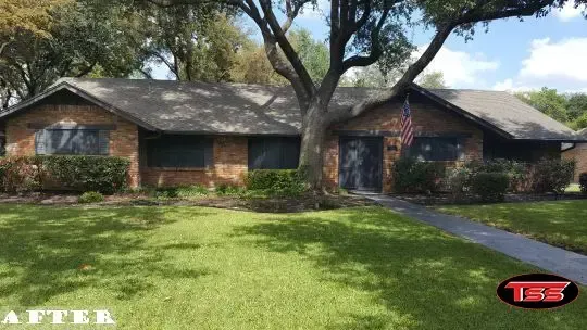 A brick house with a lush green lawn and a tree in front of it.