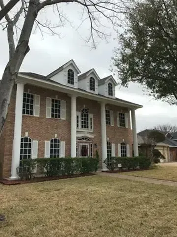 A large brick house with white columns and shutters is sitting on top of a lush green lawn.